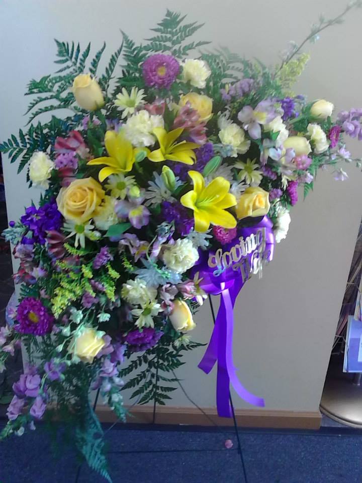 Large standing floral spray with yellow lilies, roses, and purple blooms