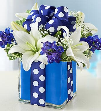 White lilies and blue flowers in a blue gift box with a polka-dot ribbon bow