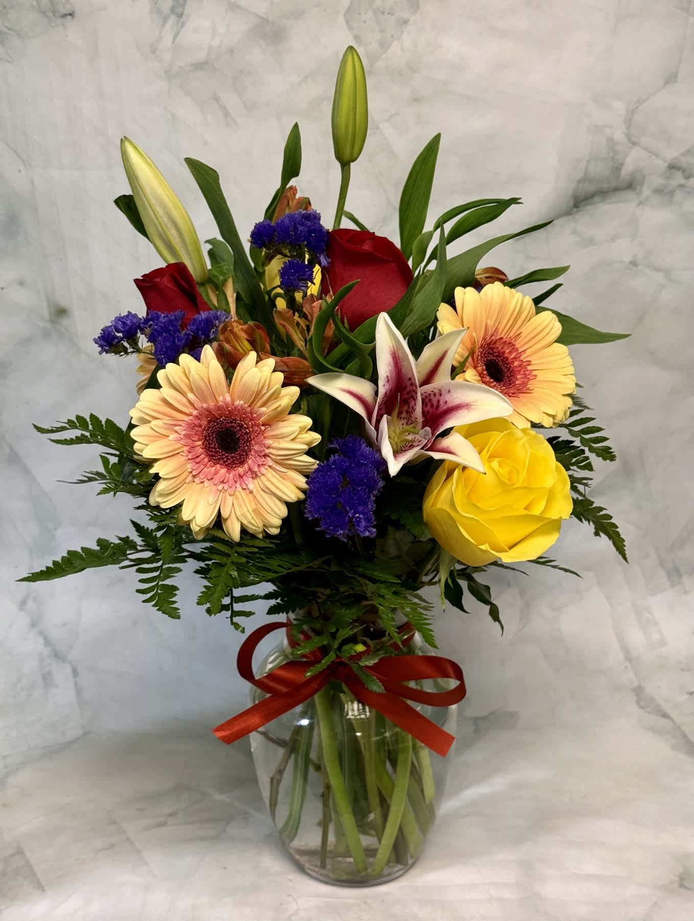 Mixed bouquet in a glass vase with lilies, roses, and gerbera daisies