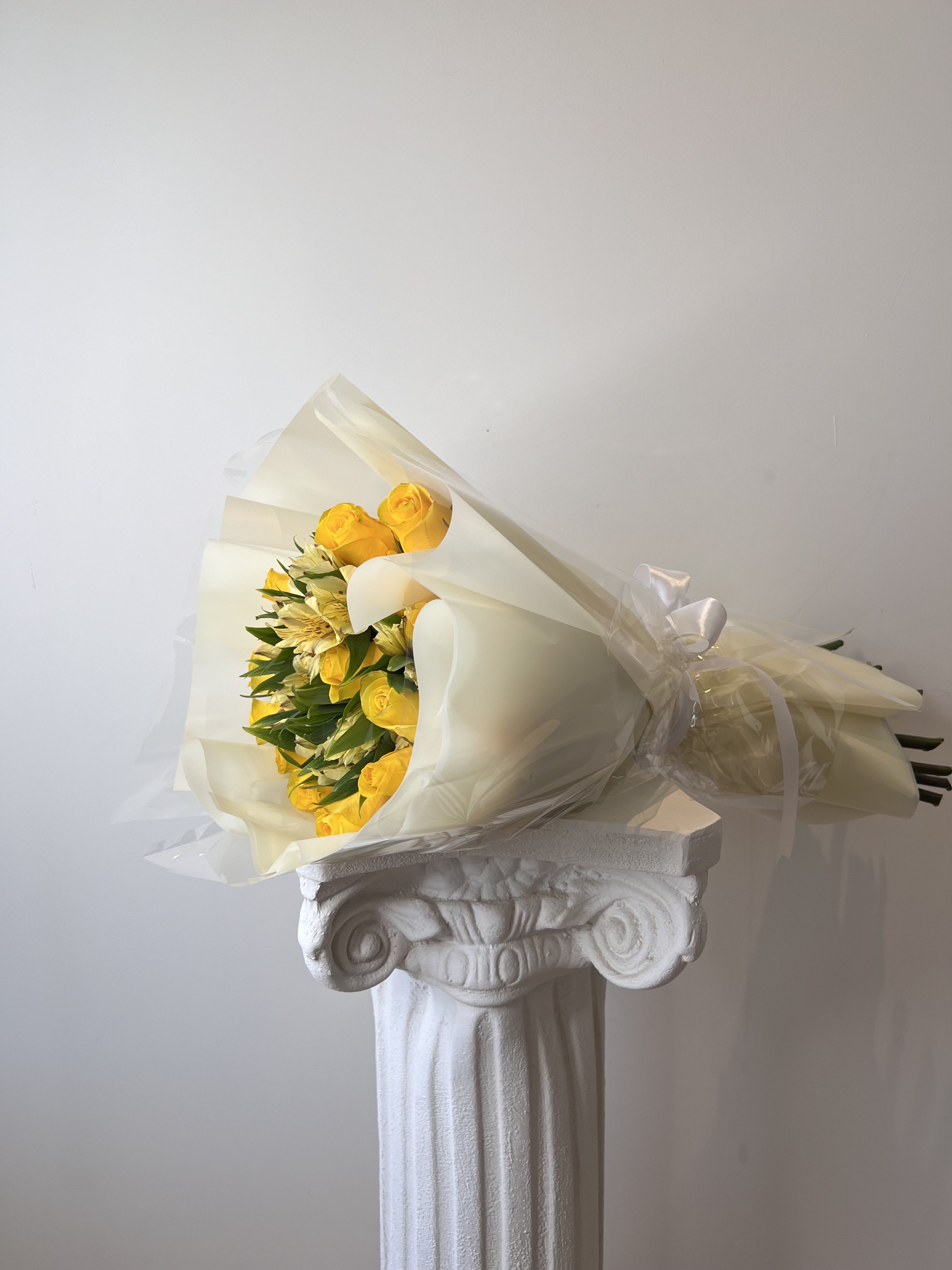 Bouquet of yellow roses and pale flowers wrapped in cream paper