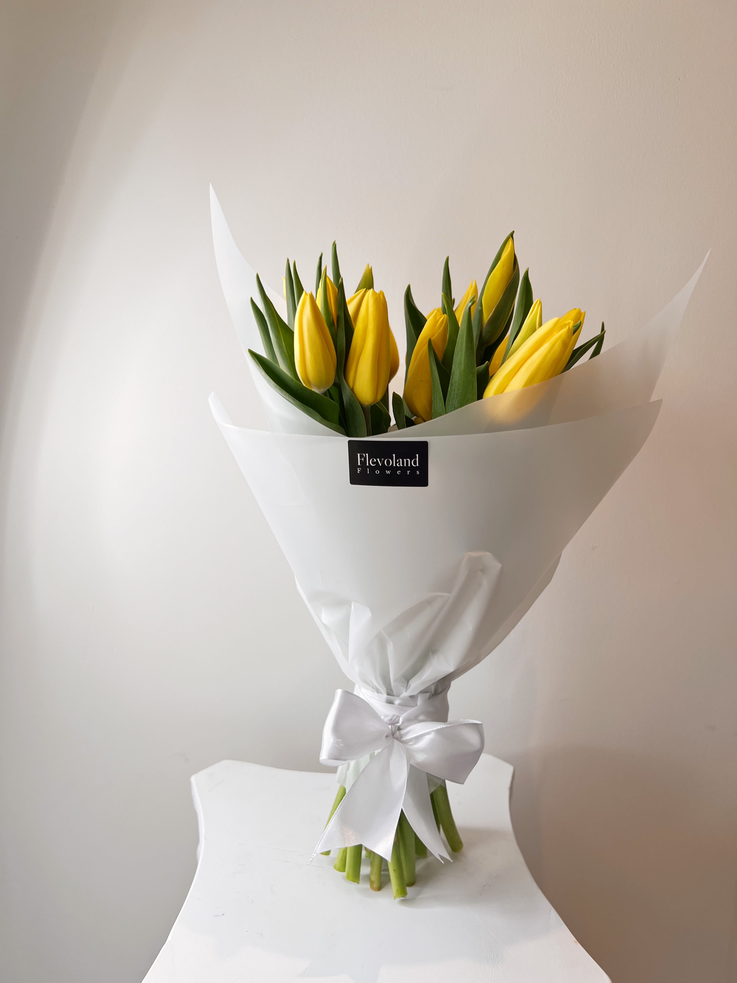 Bouquet of yellow tulips wrapped in white paper with a satin bow