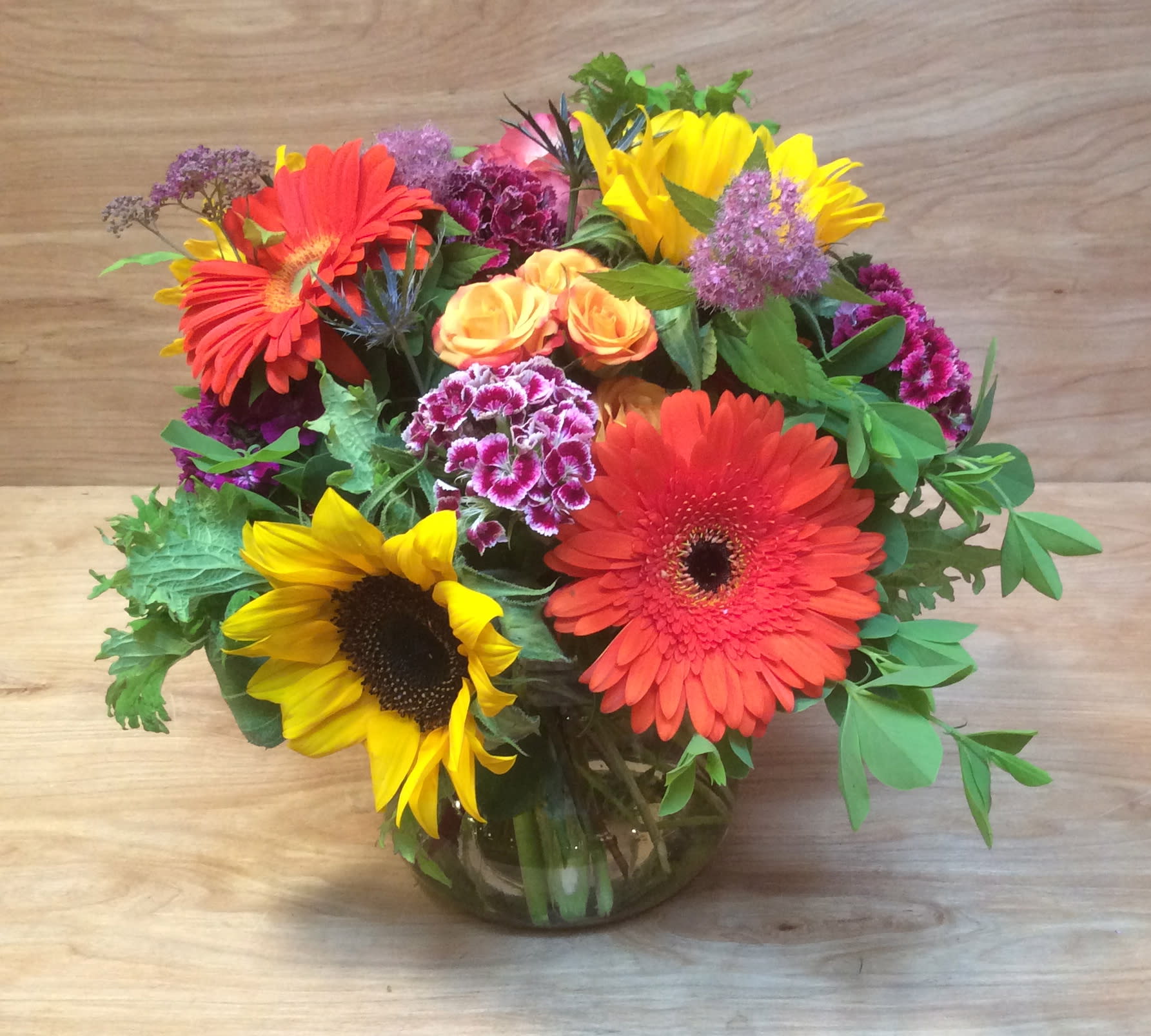 Mixed bouquet with sunflowers, gerbera daisies, roses, and carnations in a glass vase
