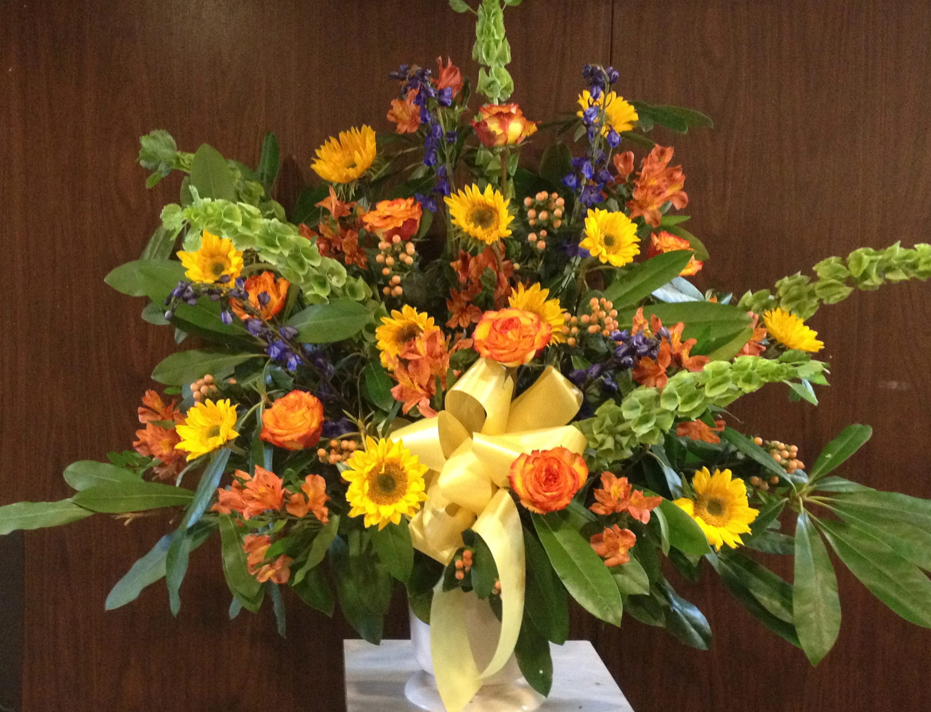 Large mixed bouquet with yellow sunflowers, orange roses, and a yellow ribbon in a vase