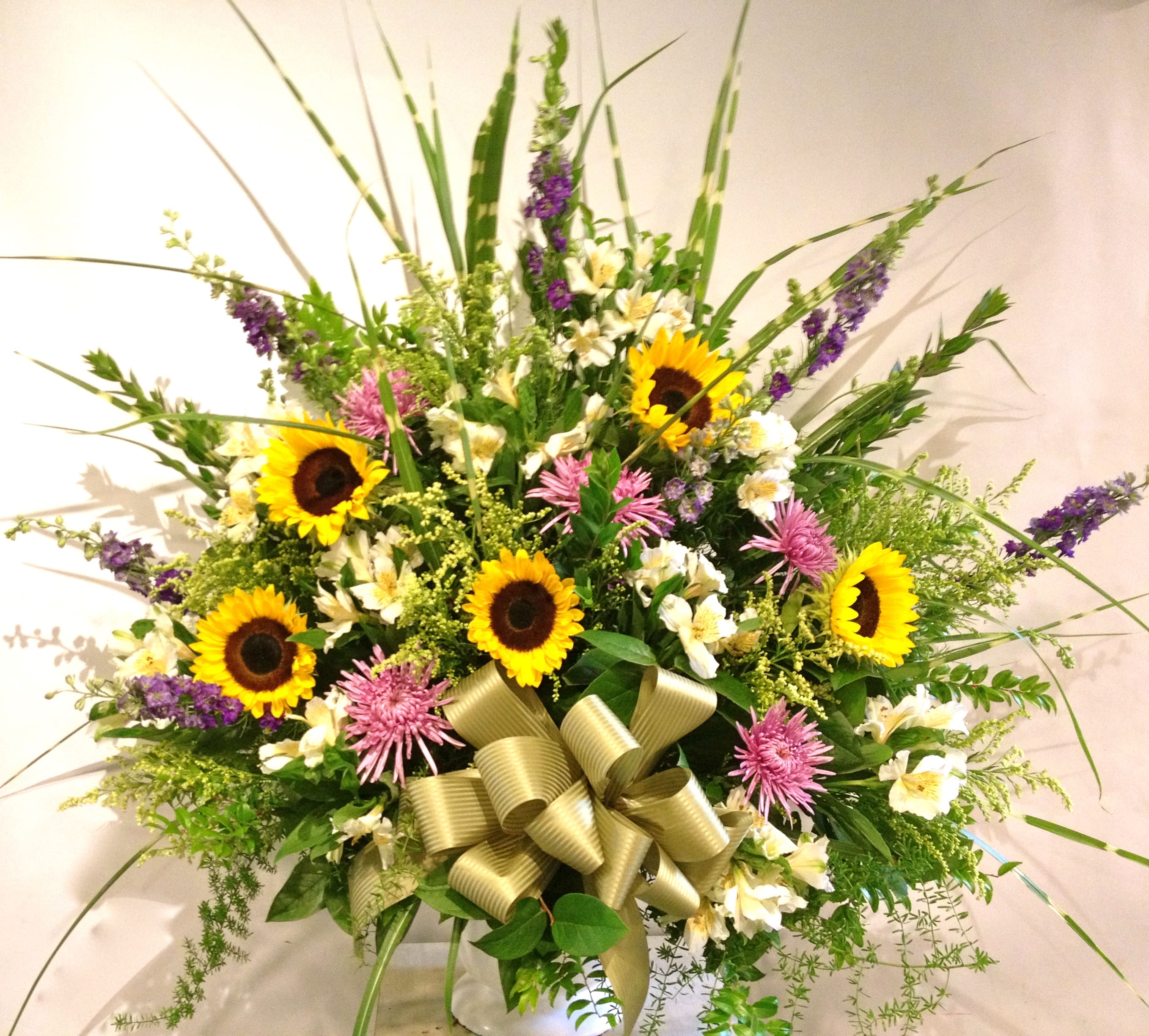 Large mixed bouquet with sunflowers, pink blooms, and a gold ribbon