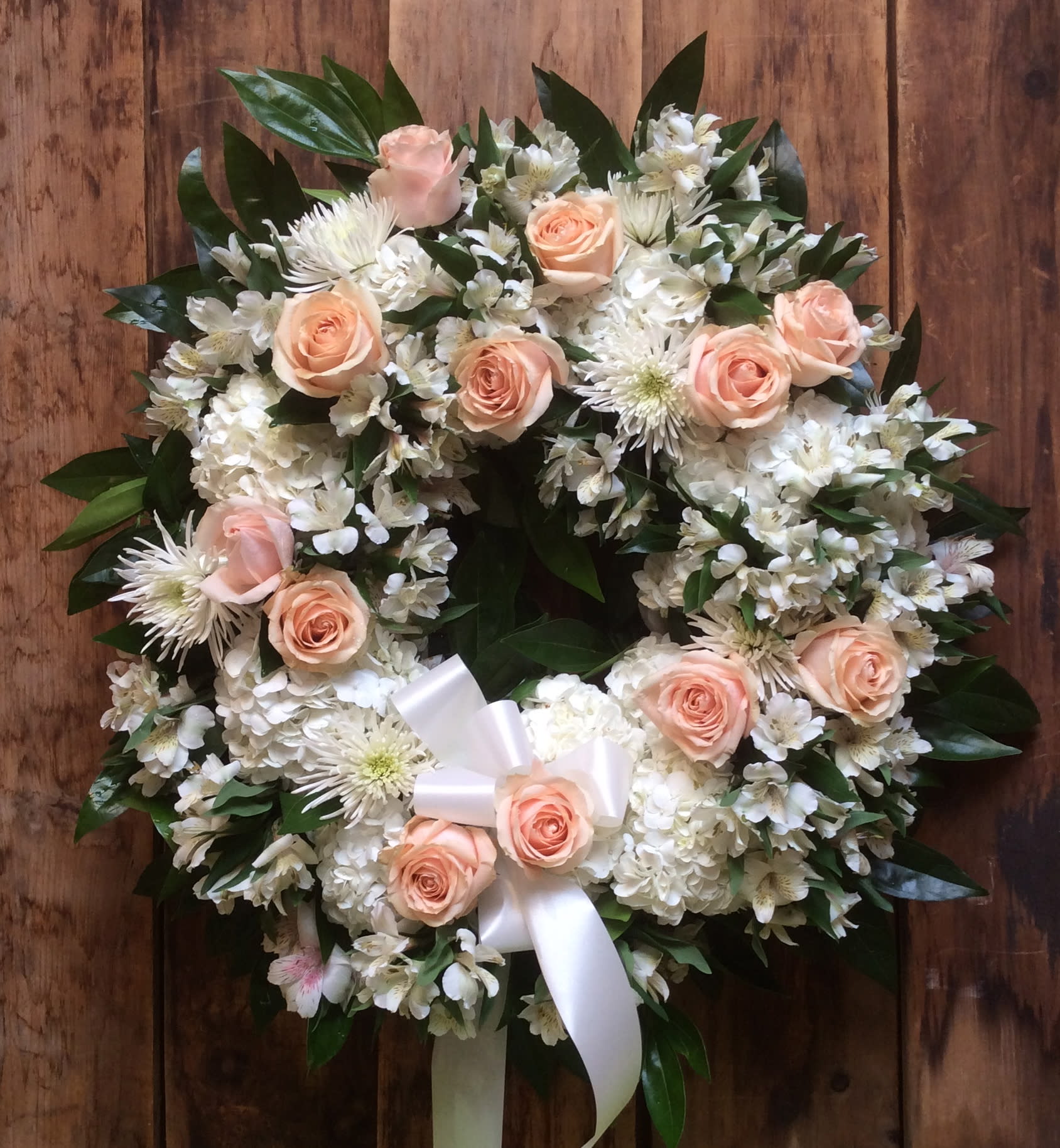Round floral wreath with peach roses and white flowers on a wooden background