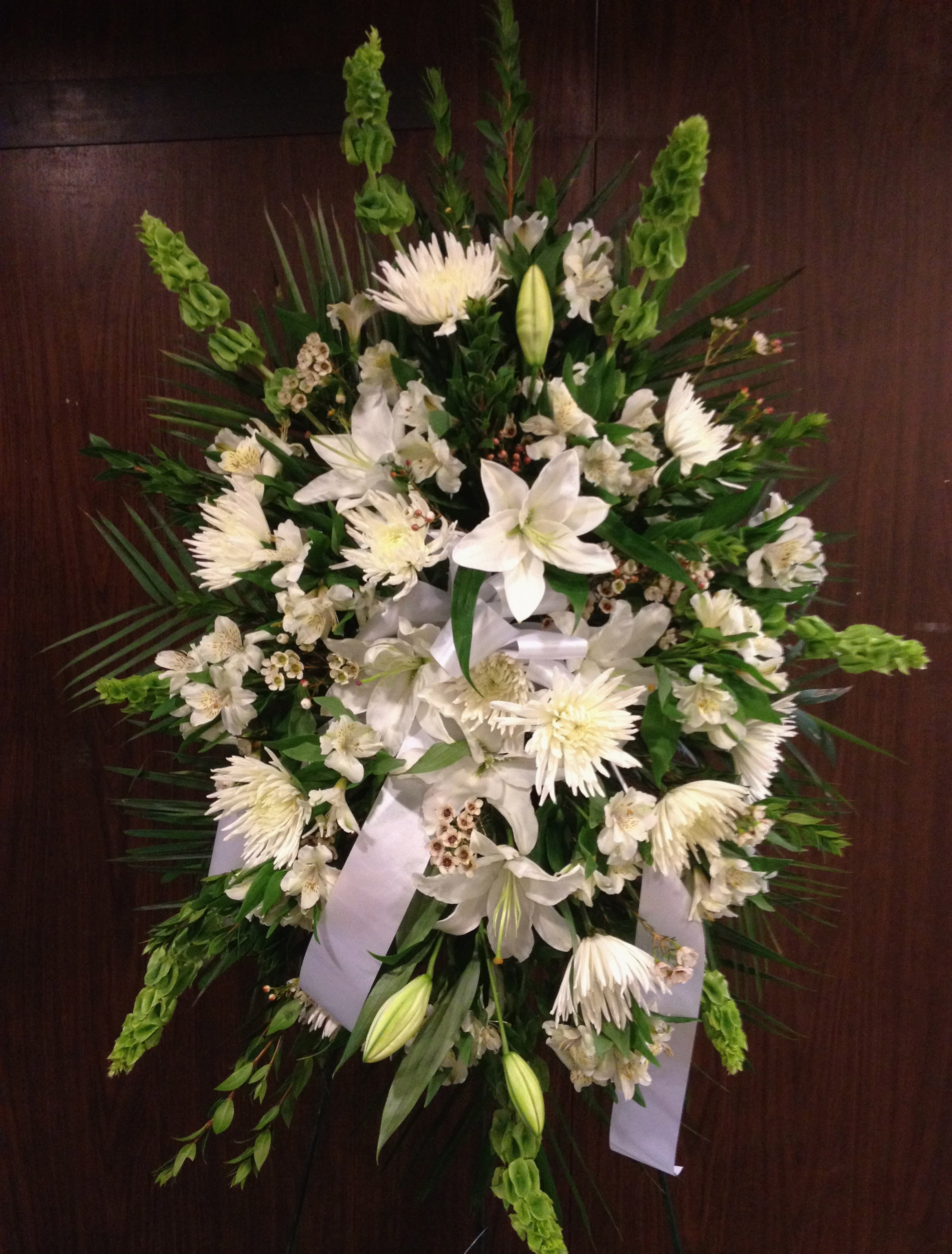 White funeral spray with lilies, chrysanthemums, and ribbon