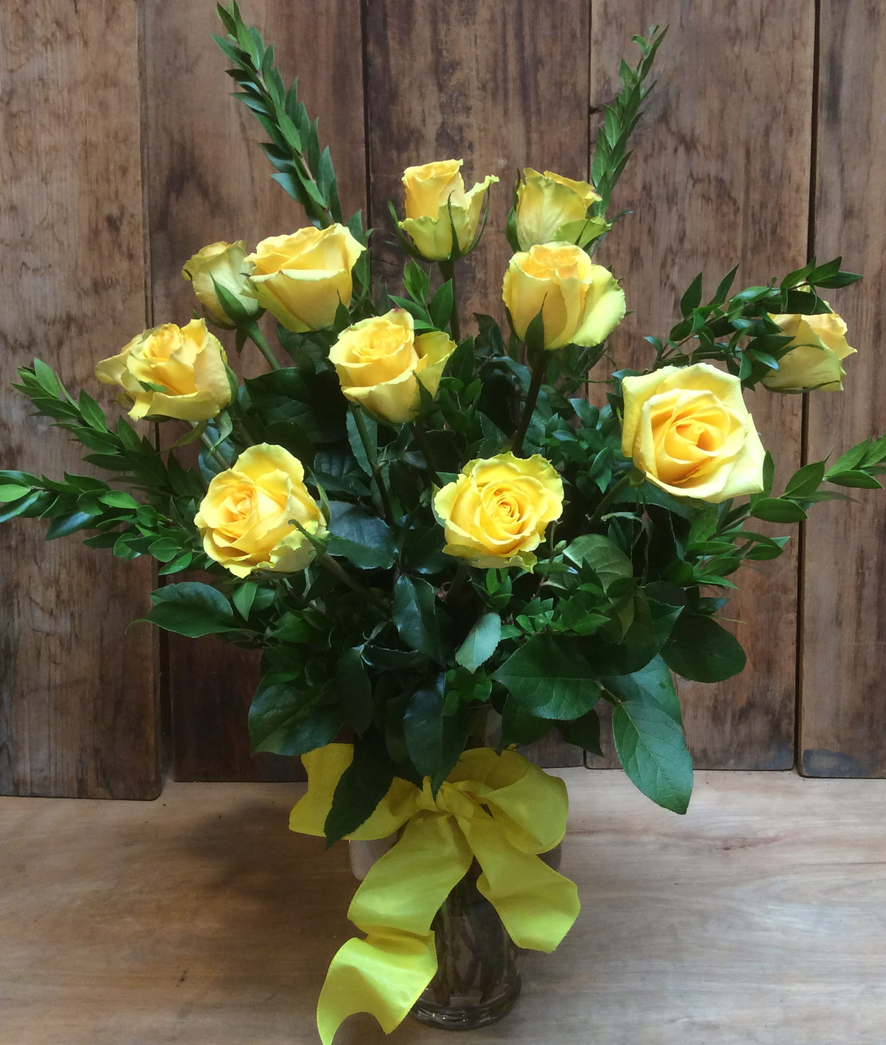 Yellow roses arranged in a glass vase with a yellow ribbon