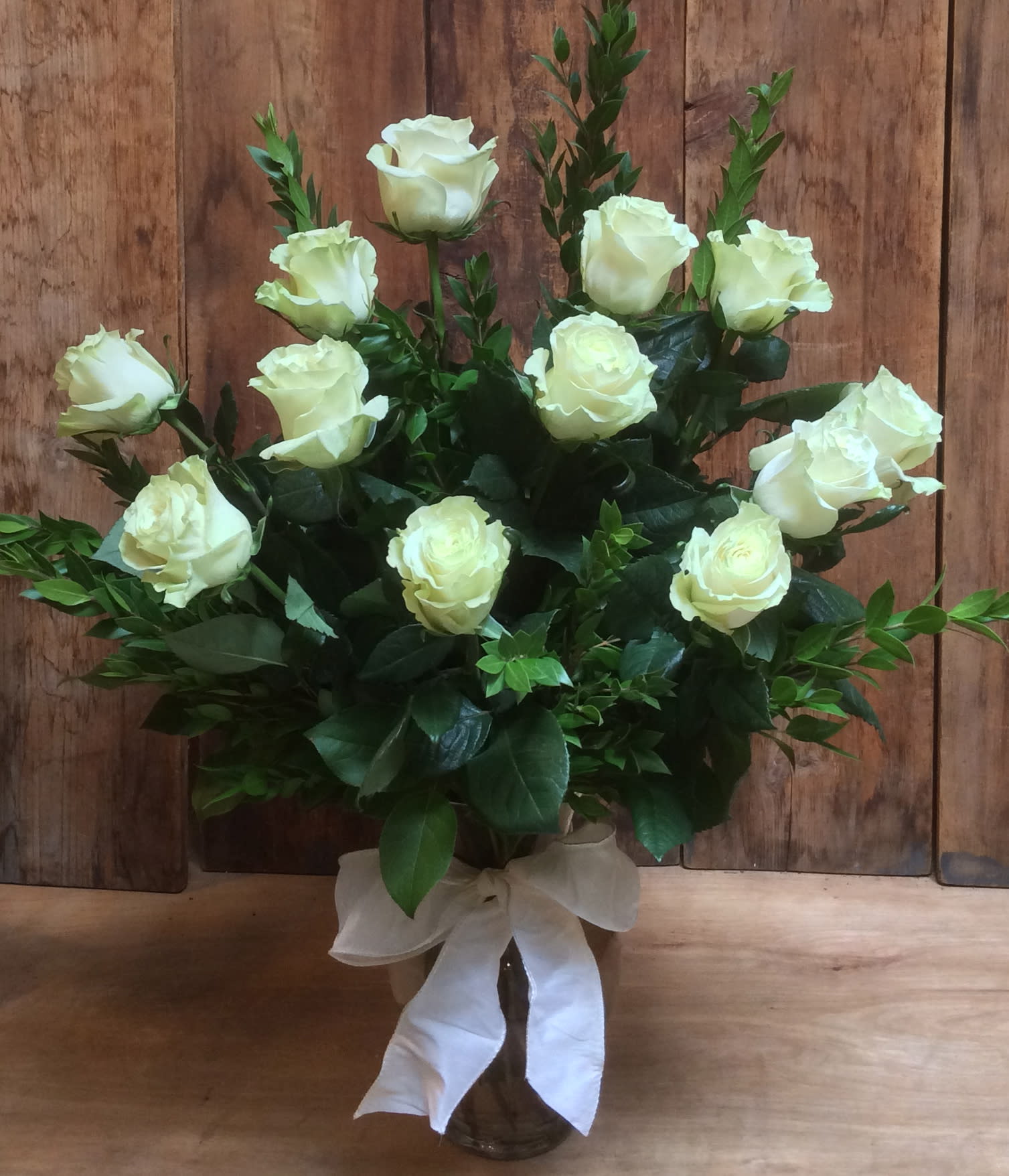 White roses arranged in a glass vase with a white ribbon