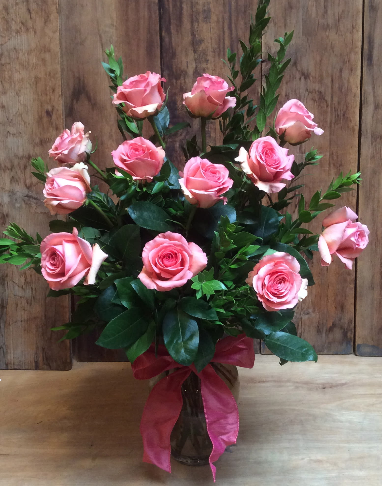 Pink roses arranged in a glass vase with a pink ribbon