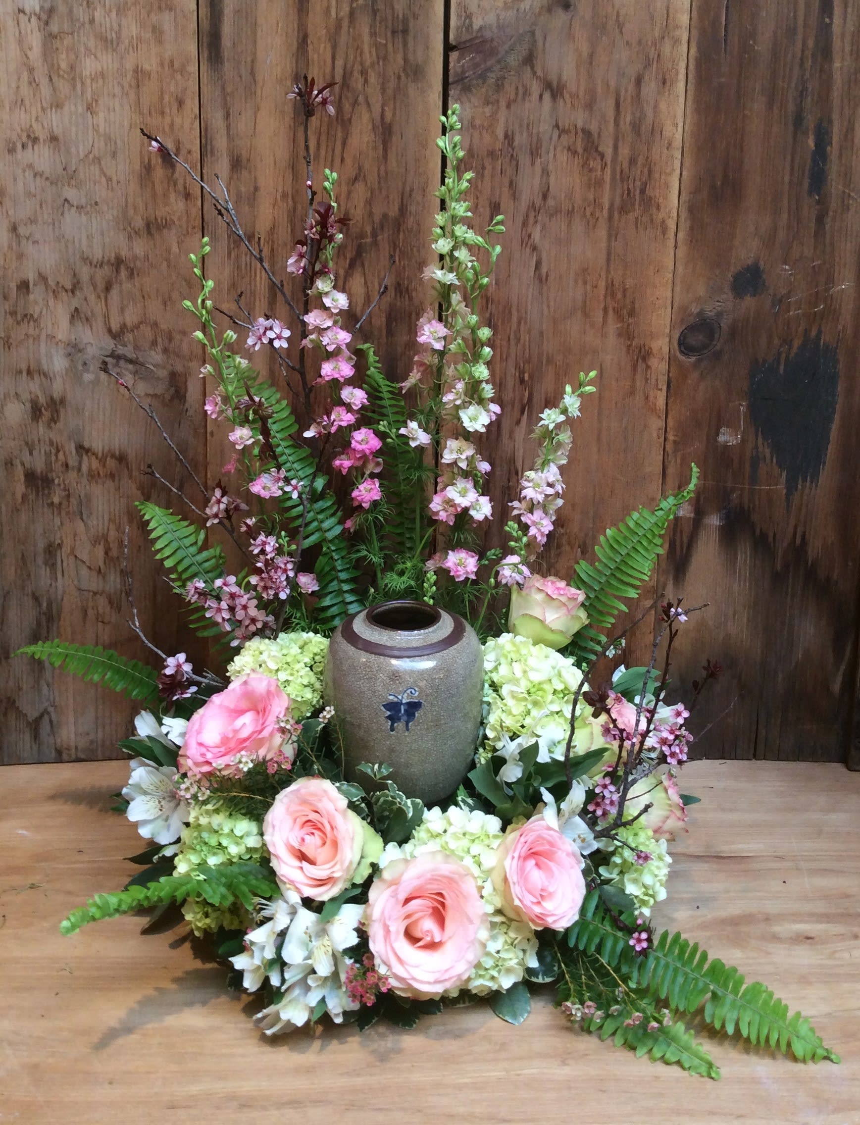 Pink roses and white flowers arranged around a ceramic urn