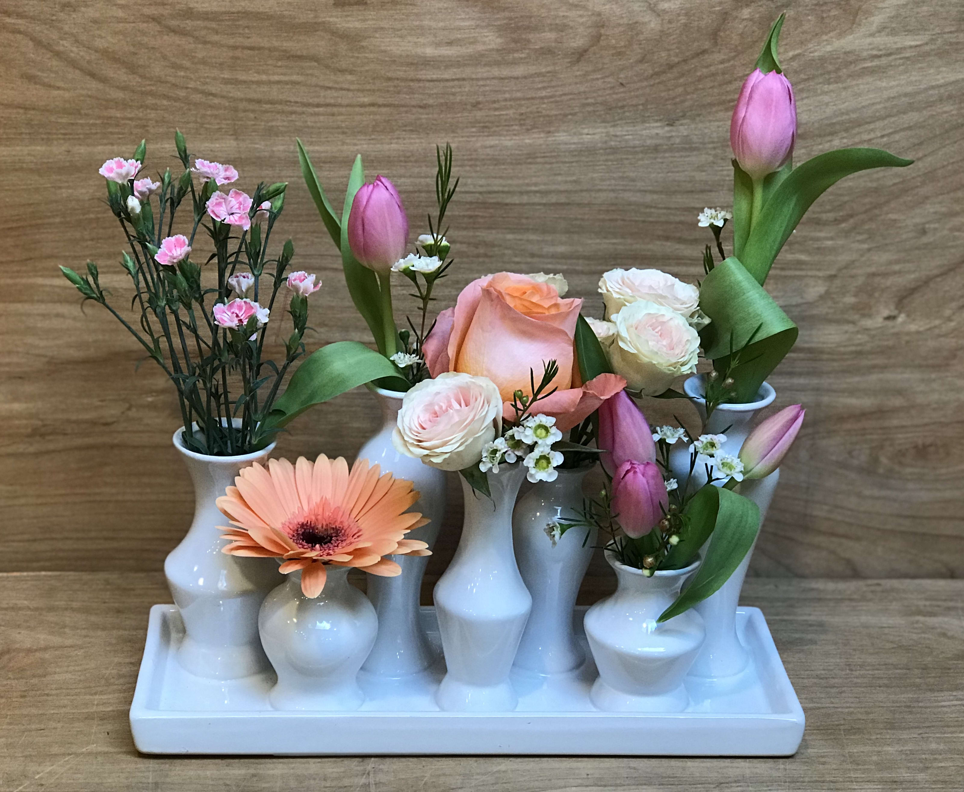 Floral arrangement in white bud vases with pink tulips, roses, and a peach gerbera daisy