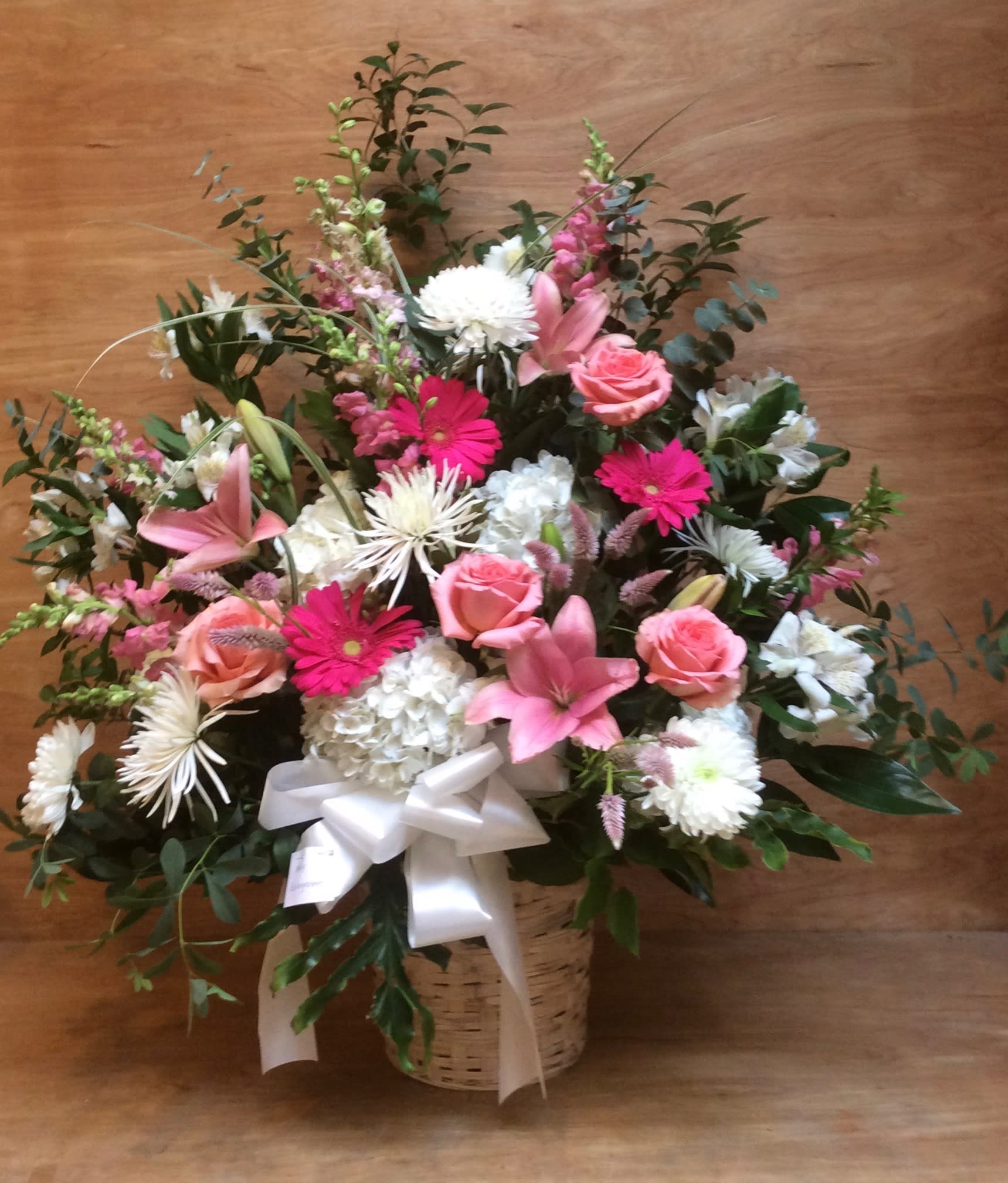 Pink and white mixed flower arrangement in a basket with a white ribbon
