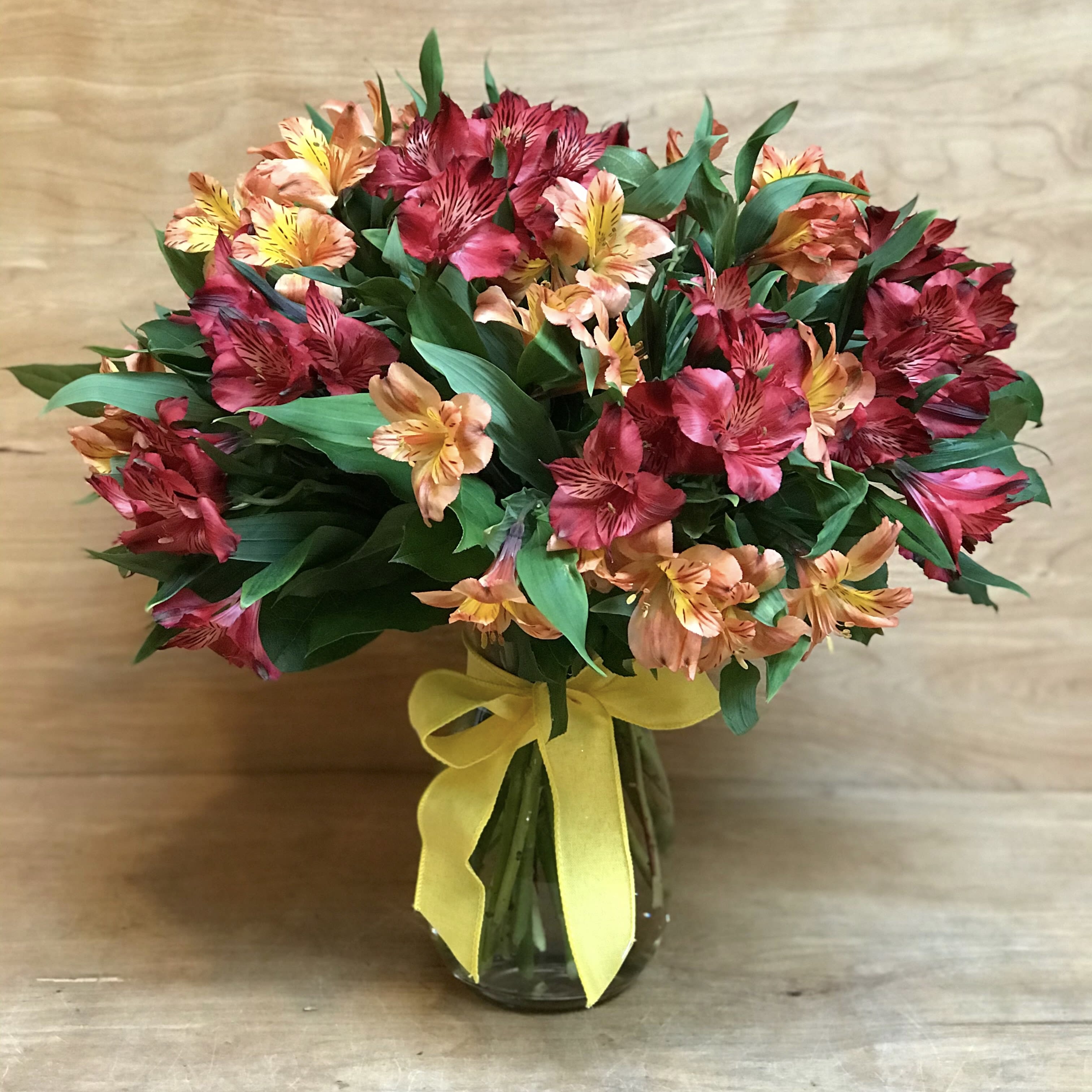 Bouquet of red and peach flowers in a glass vase with a yellow ribbon
