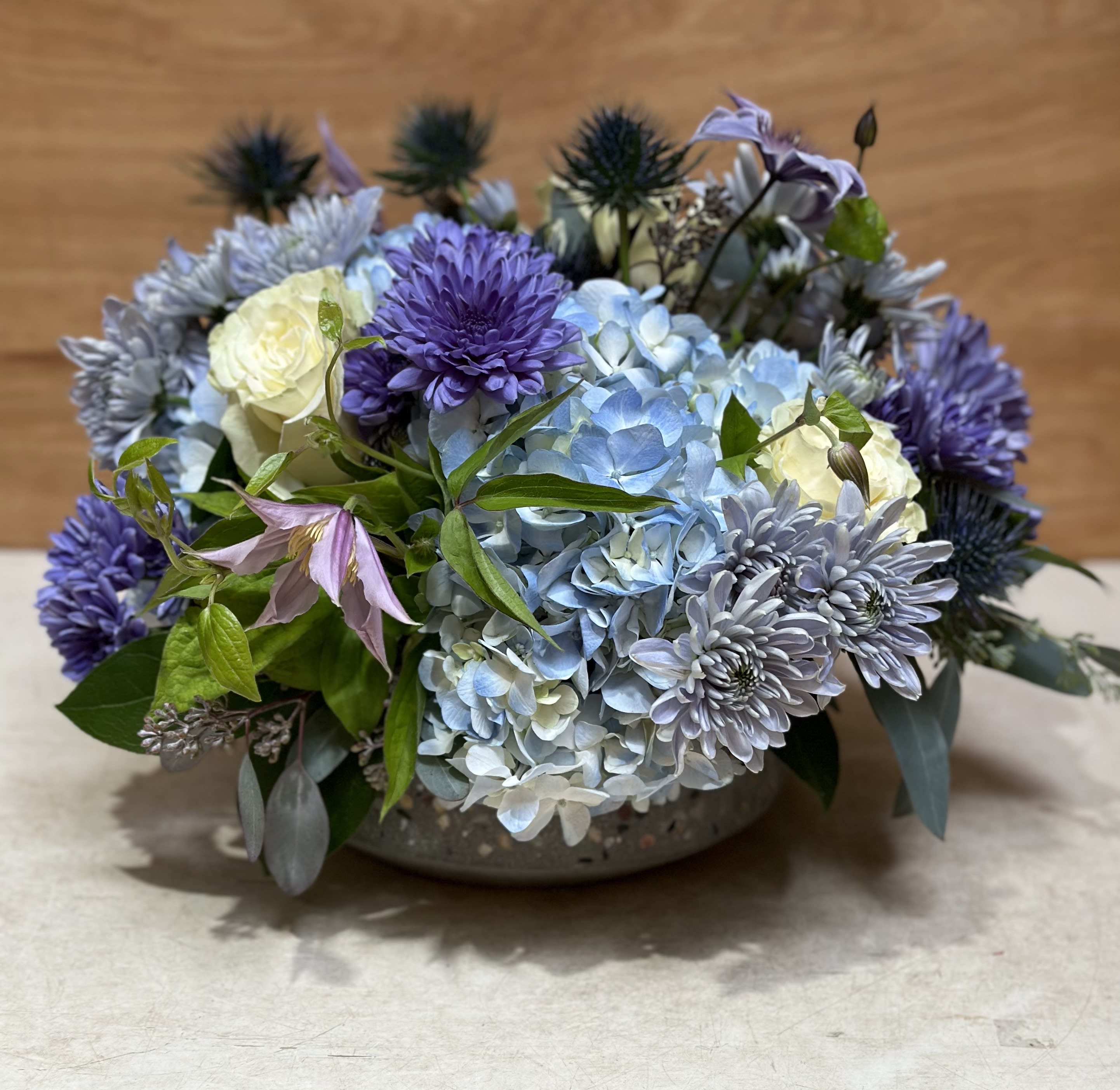 Low arrangement of blue hydrangeas, purple mums, and white roses in a shallow bowl