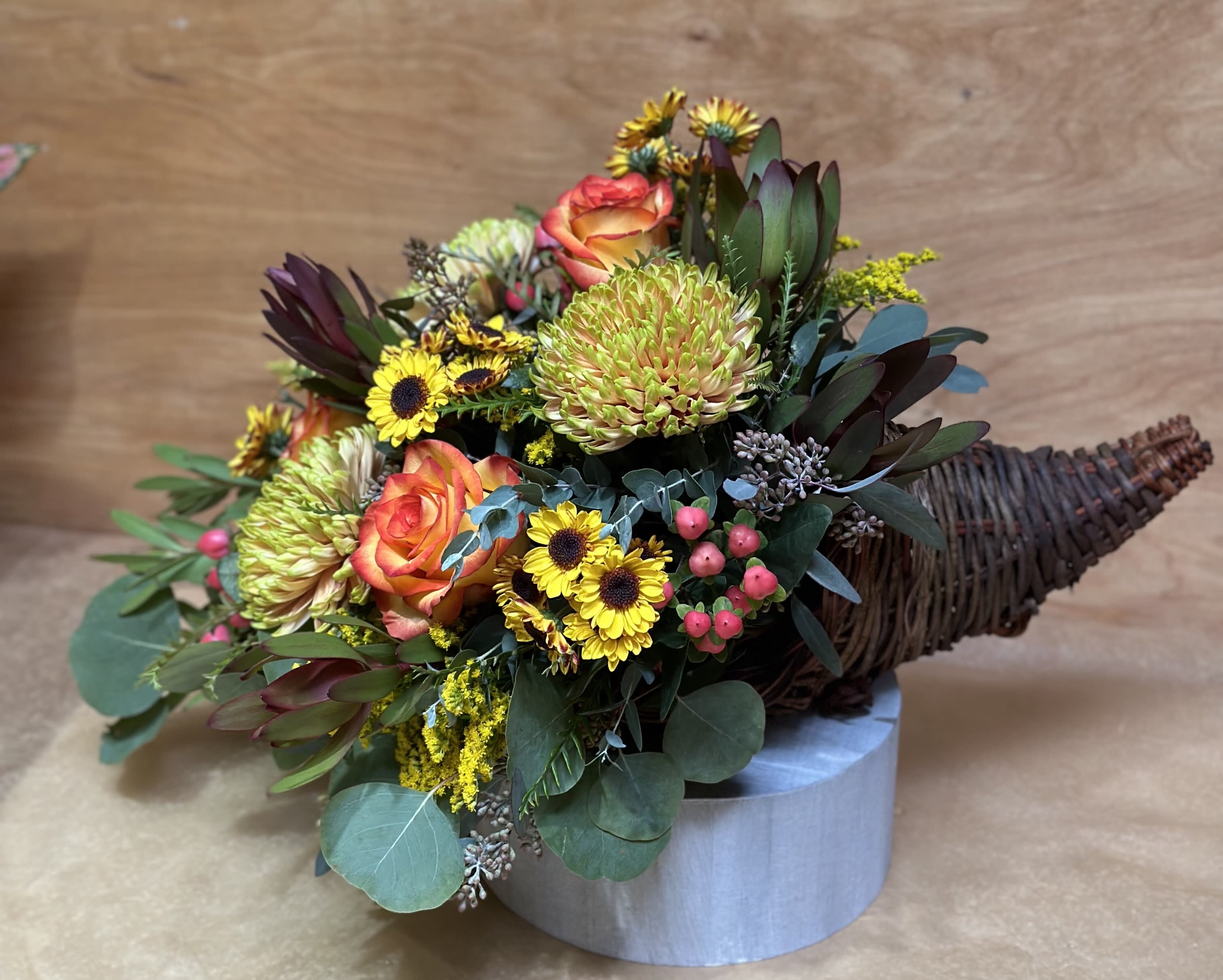 Mixed bouquet with orange roses, yellow blooms, and dark foliage in a wicker cone