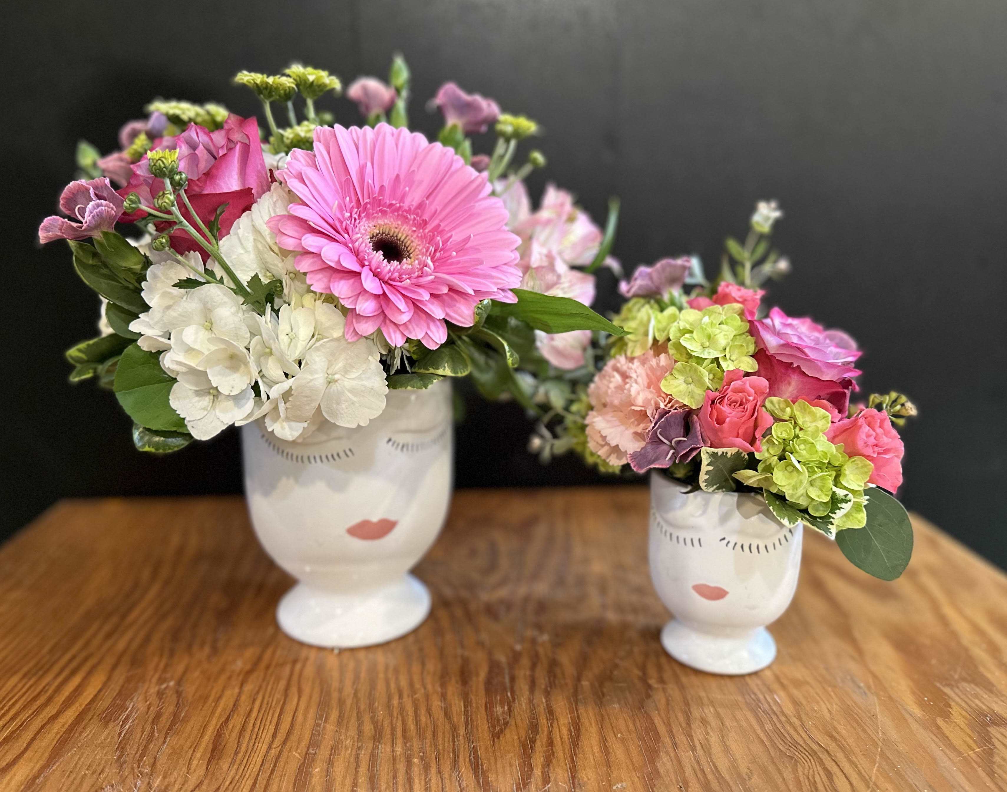 Two floral arrangements in white face vases on a wooden table