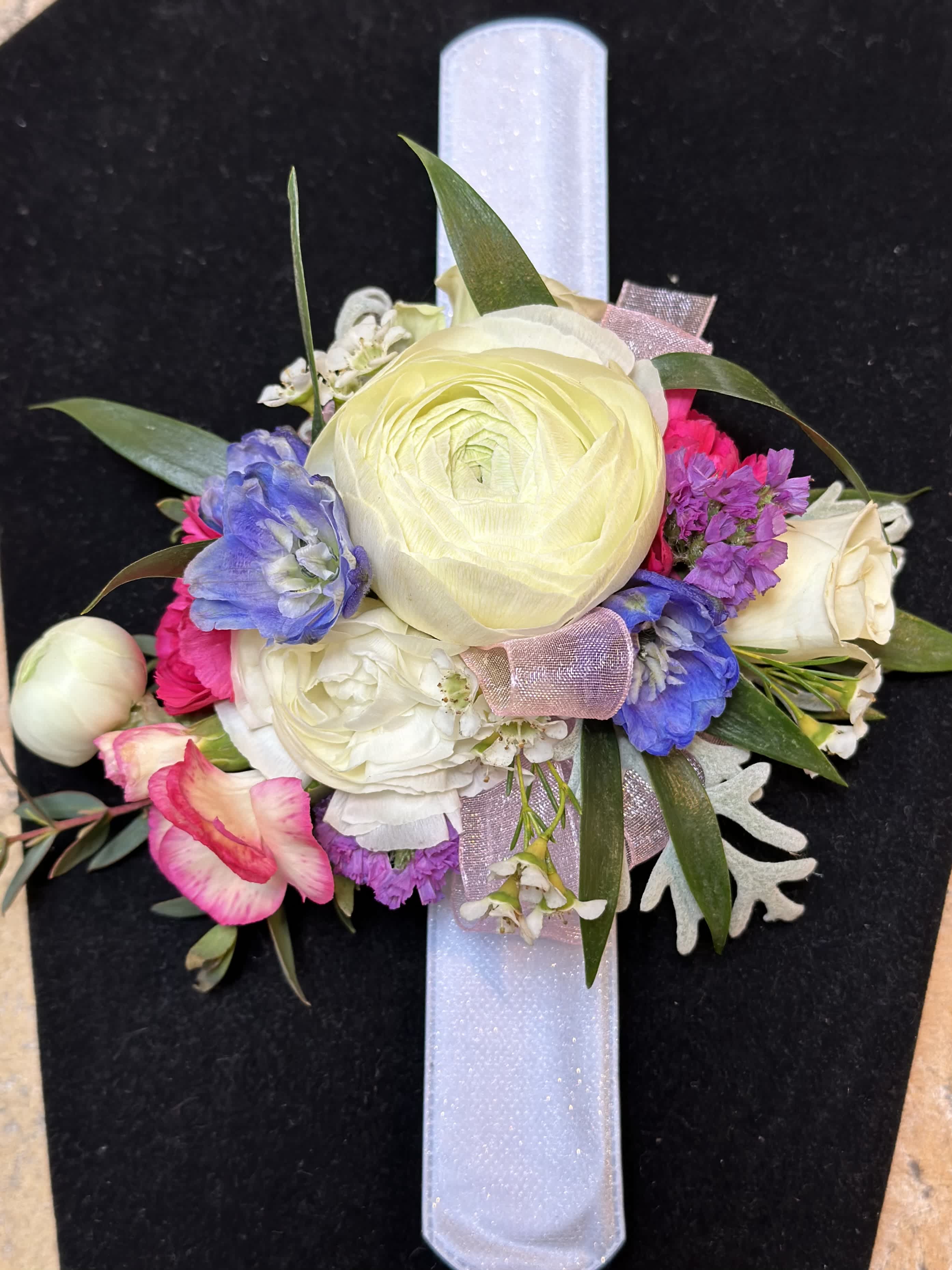 Floral wrist corsage with cream, pink, and purple blooms on a white band