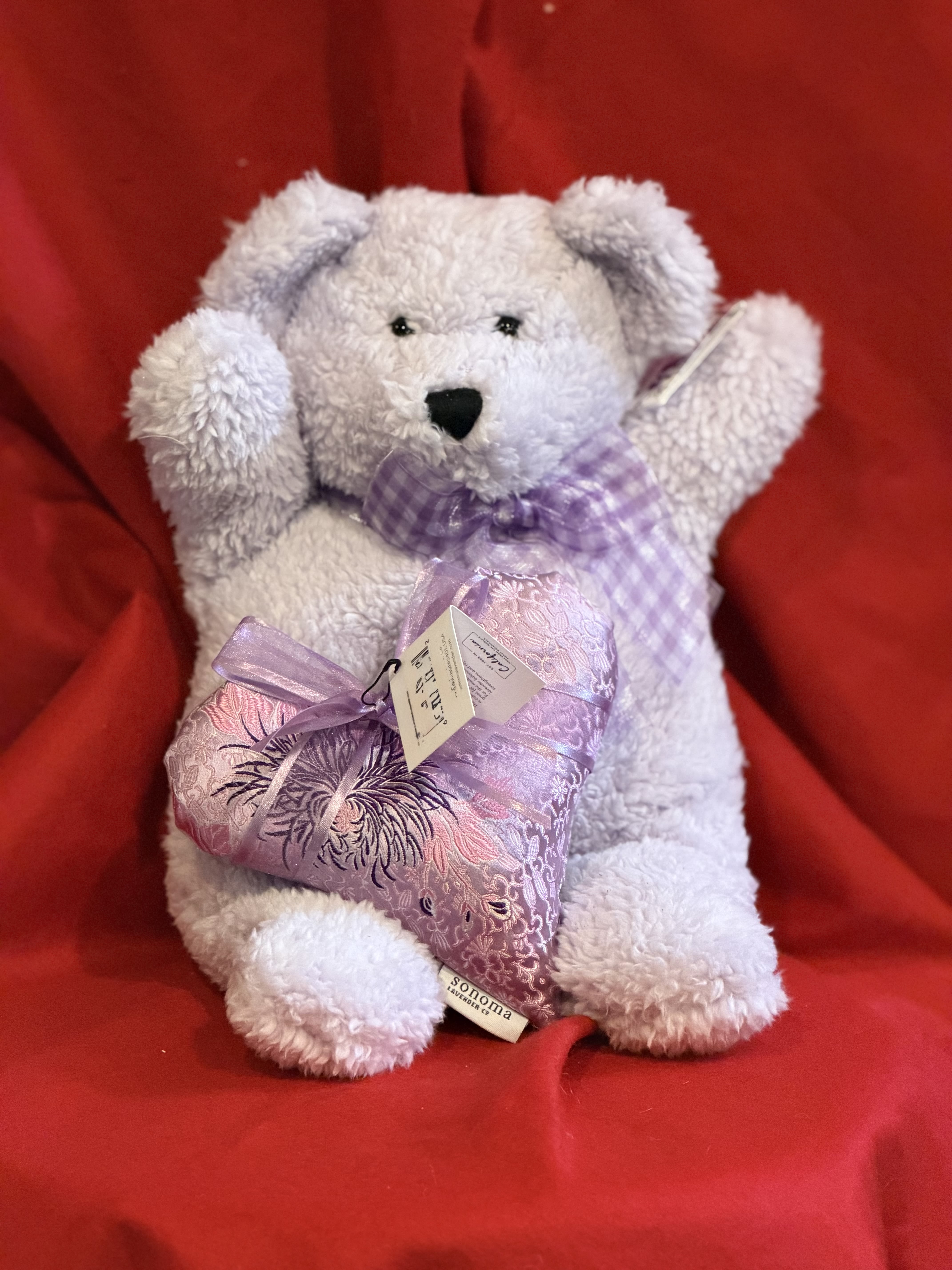 White teddy bear holding a lavender heart pillow on a red background