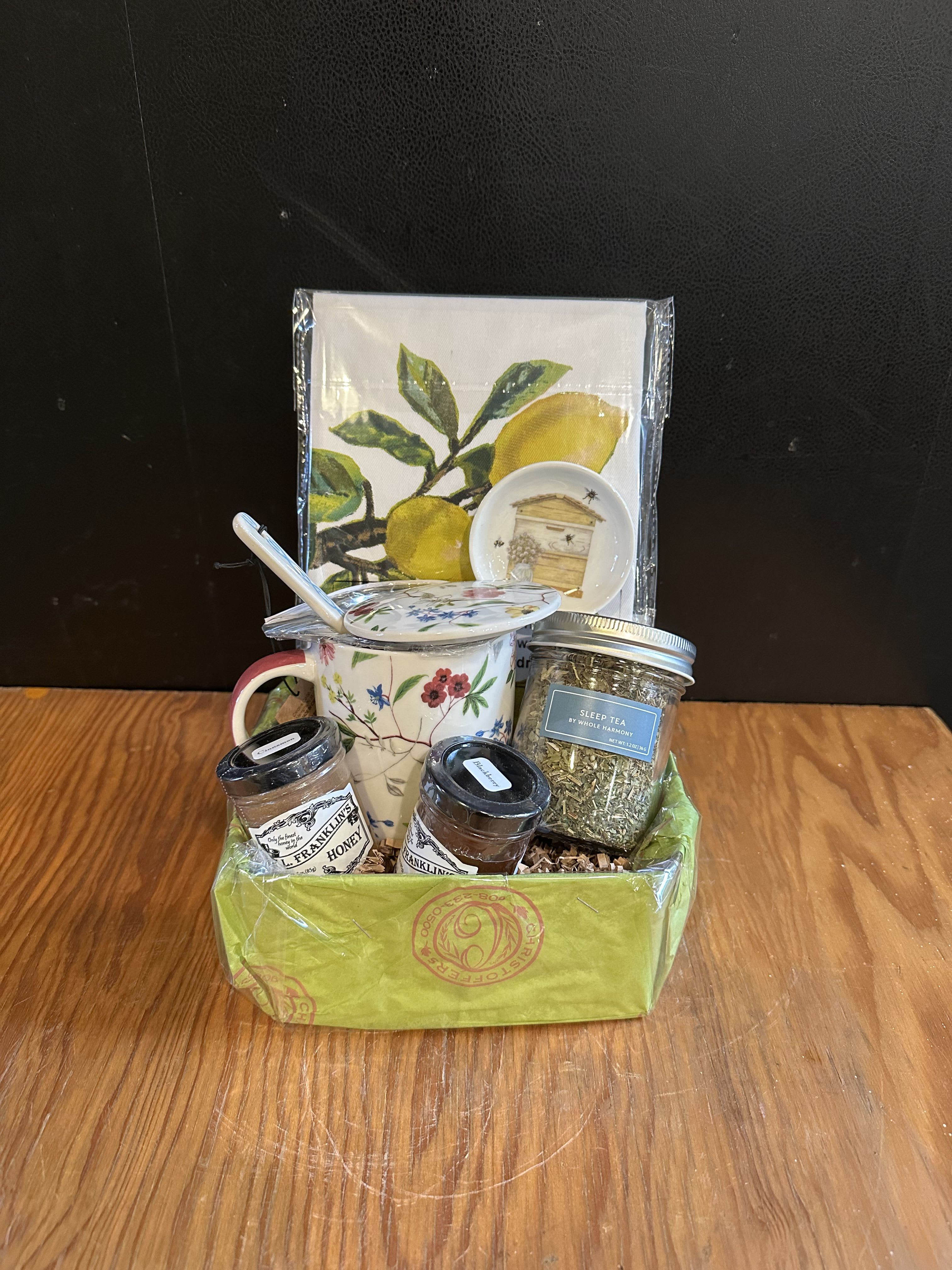 Tea Lover's Basket - A charming collection for tea enthusiasts, featuring soothing sleep tea, gourmet honey, a floral tea mug with lid &amp; strainer and a beautiful kitchen towel. Perfect for cozy moments of a beautifully curated gift.