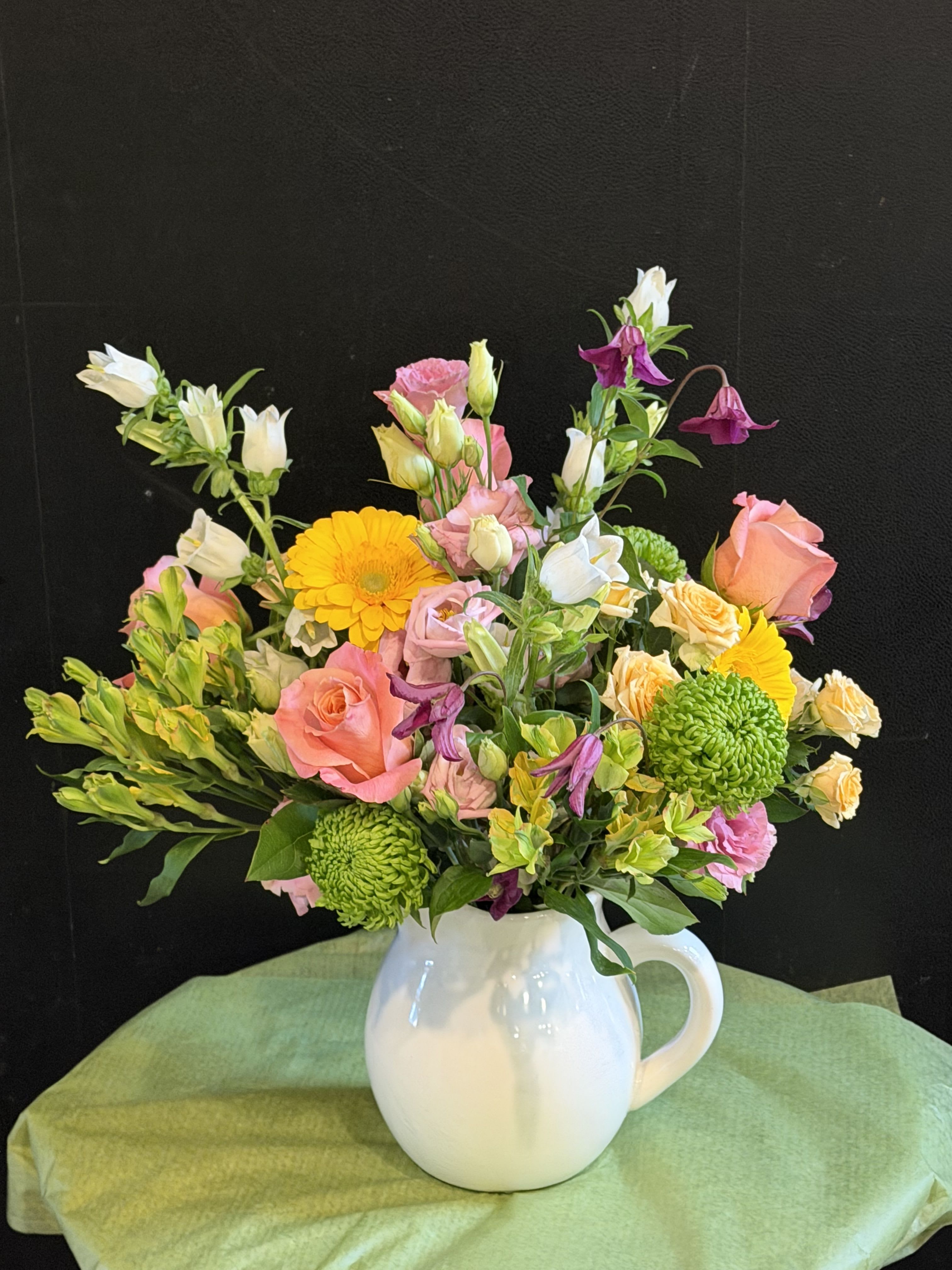 Wildflower Whimsy  - A cheerful mix of soft pinks, sunny yellows, fresh greens, and delicate purples nestled in a charming white ceramic pitcher. Lush blooms and airy bell-shaped accents create a whimsical, garden-fresh feel!