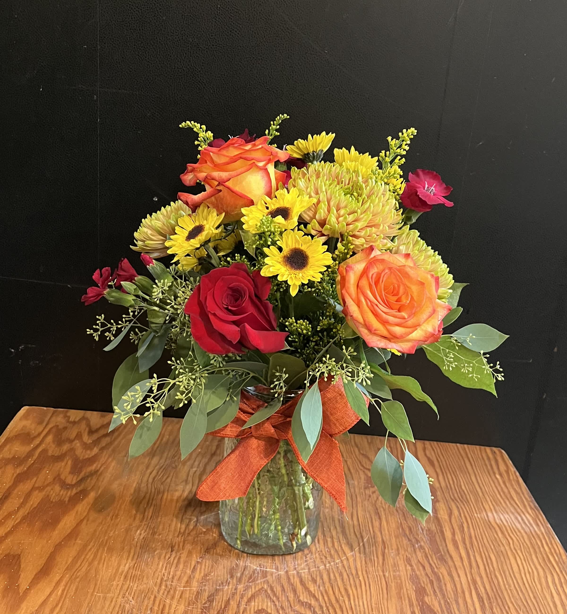 Bouquet of orange and red roses with yellow daisies in a glass vase