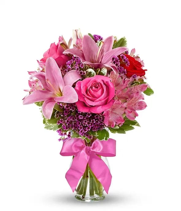 Pink roses and lilies in a glass vase with a pink ribbon