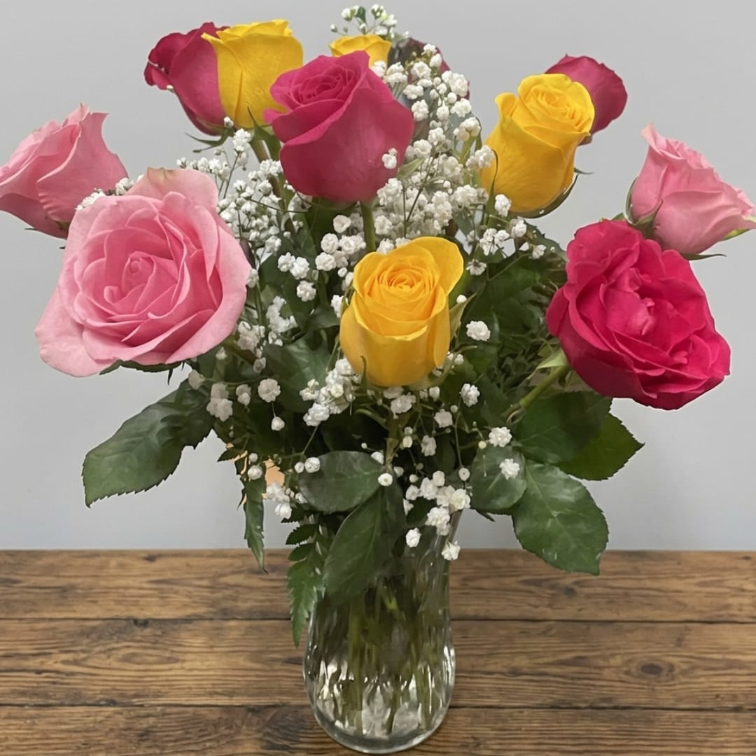 Pink and yellow roses arranged in a clear glass vase with baby's breath