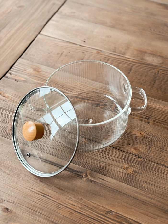 Clear glass pot with lid and wooden knob on a wooden table
