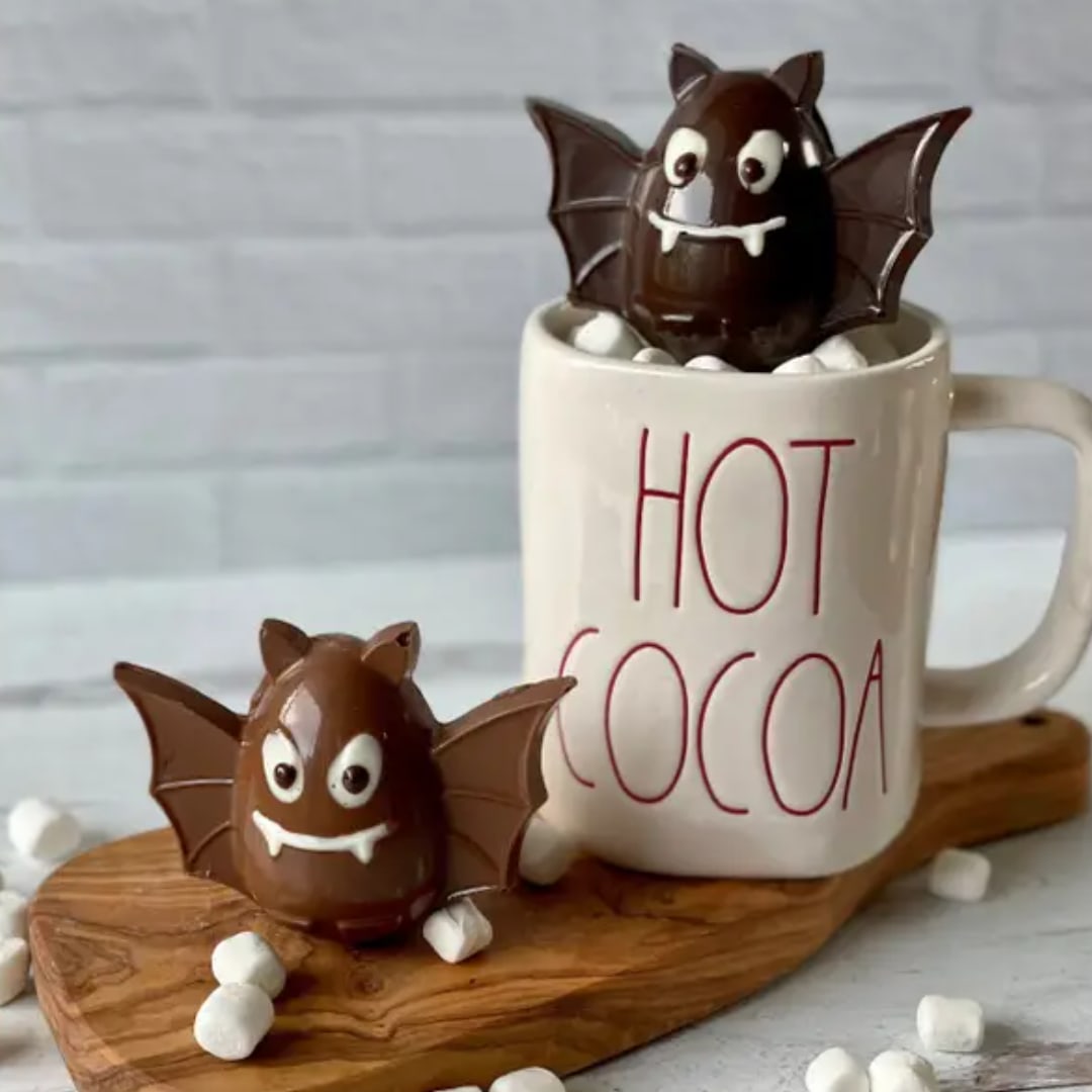 Two chocolate bat candies beside a mug labeled HOT COCOA