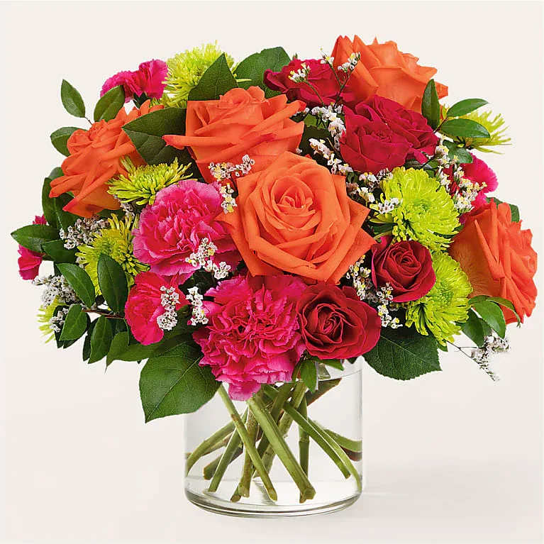 Mixed bouquet of orange, pink, and red flowers in a clear glass vase