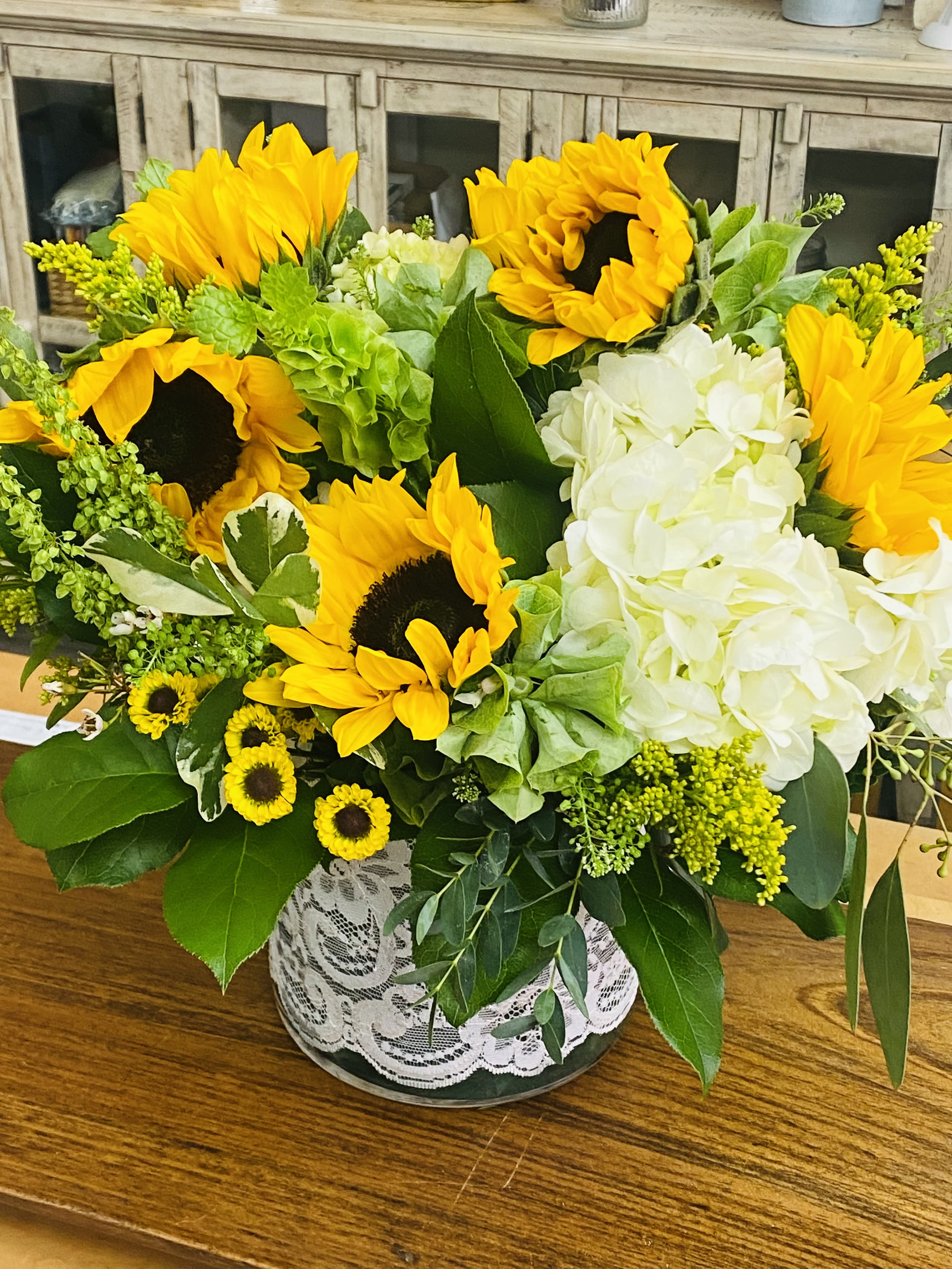 Sunflower and white hydrangea arrangement in a lace-wrapped vase