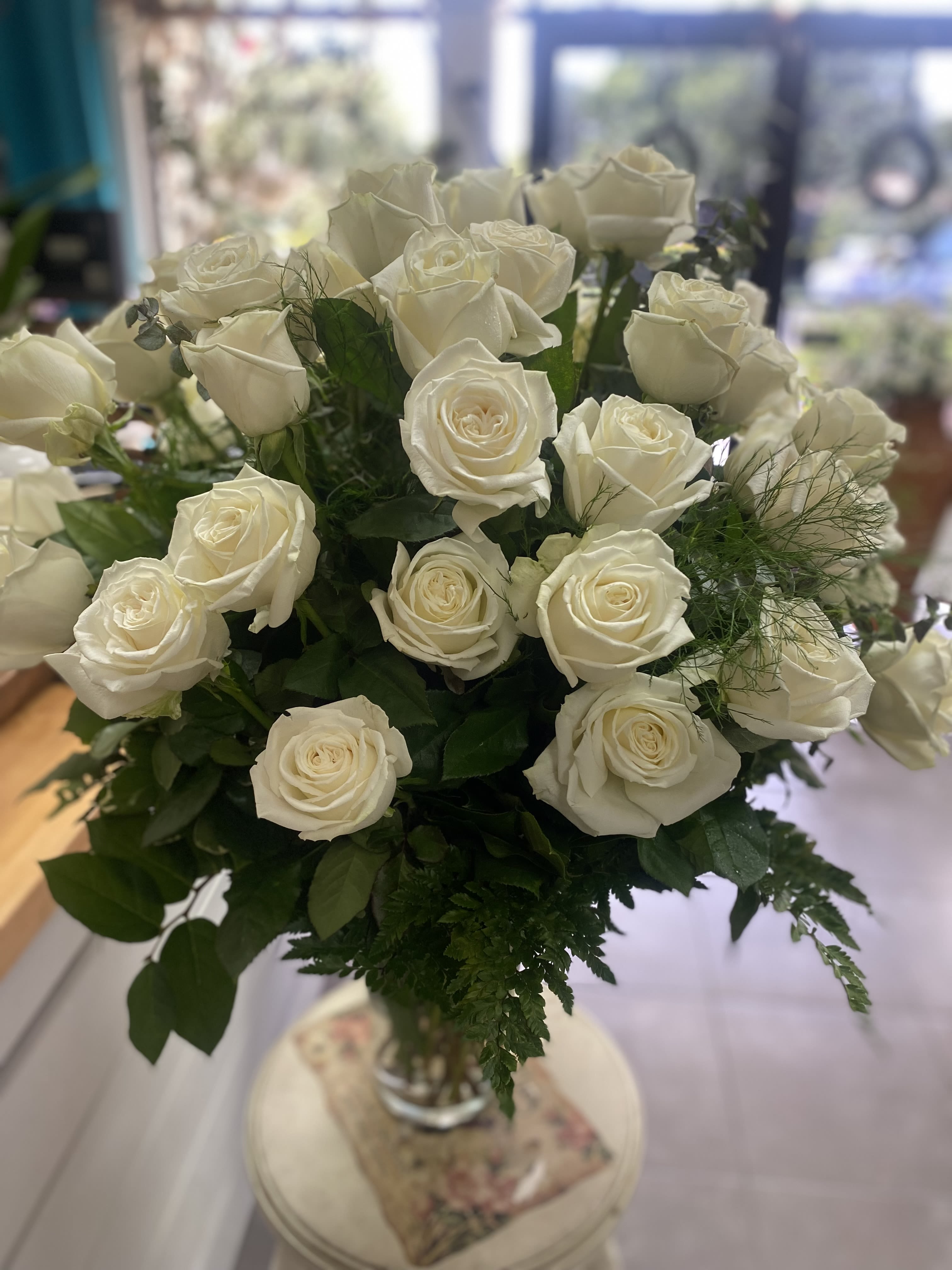 Playa Blanca - Over 2 dozen creamy white roses with lush green foliage in a clear glass vase, classic elegance