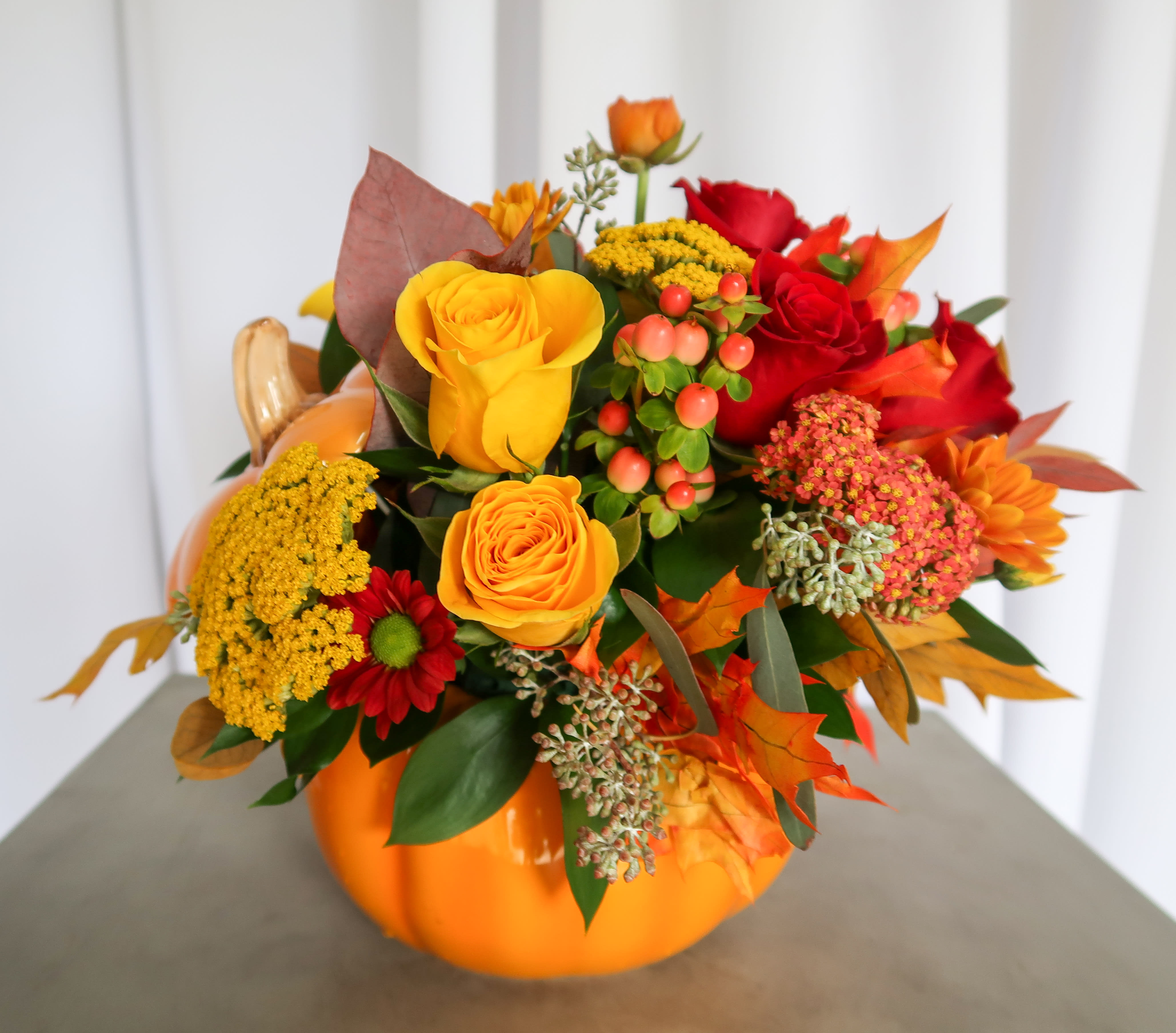Orange pumpkin vase filled with red and yellow roses and autumn flowers