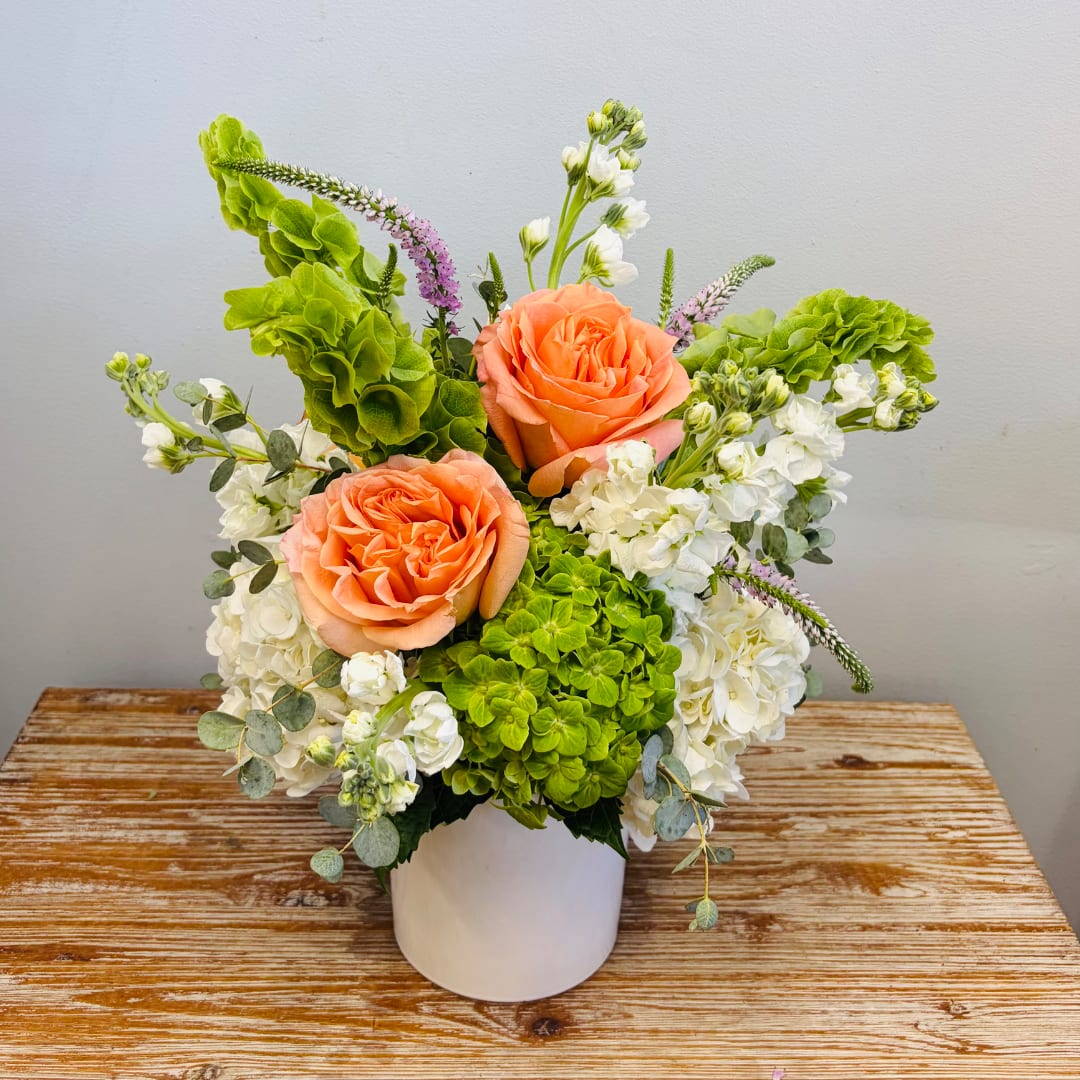 Peach roses and white flowers arranged in a white vase