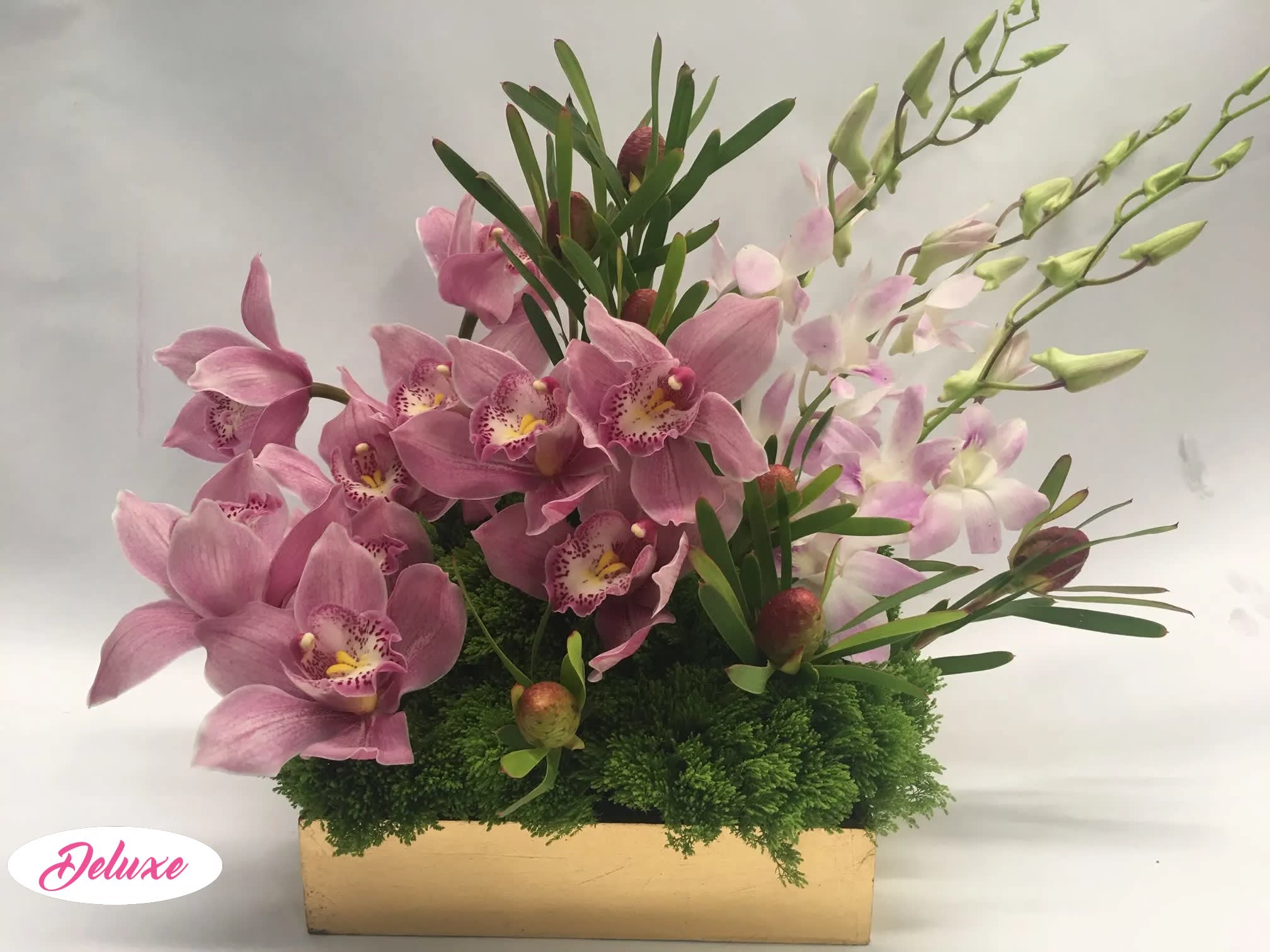 Pink orchids arranged in a rectangular box with green foliage