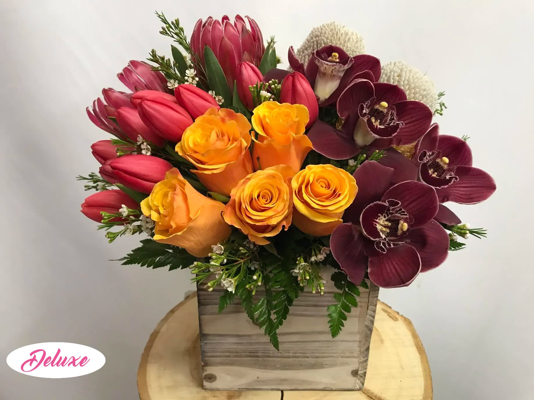 Bouquet of orange roses, red tulips, and burgundy orchids in a wooden box