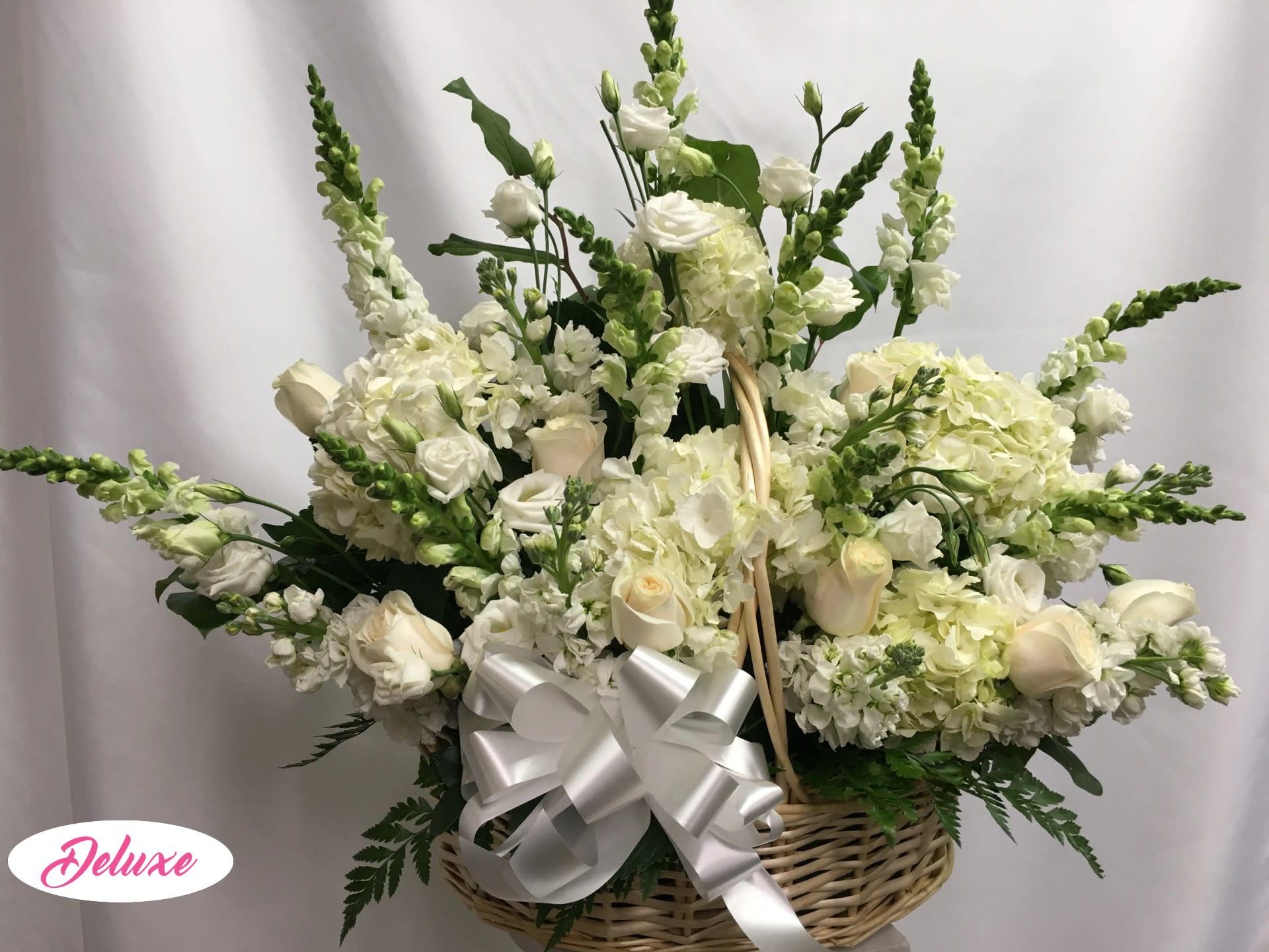 White floral arrangement in a wicker basket with a silver bow