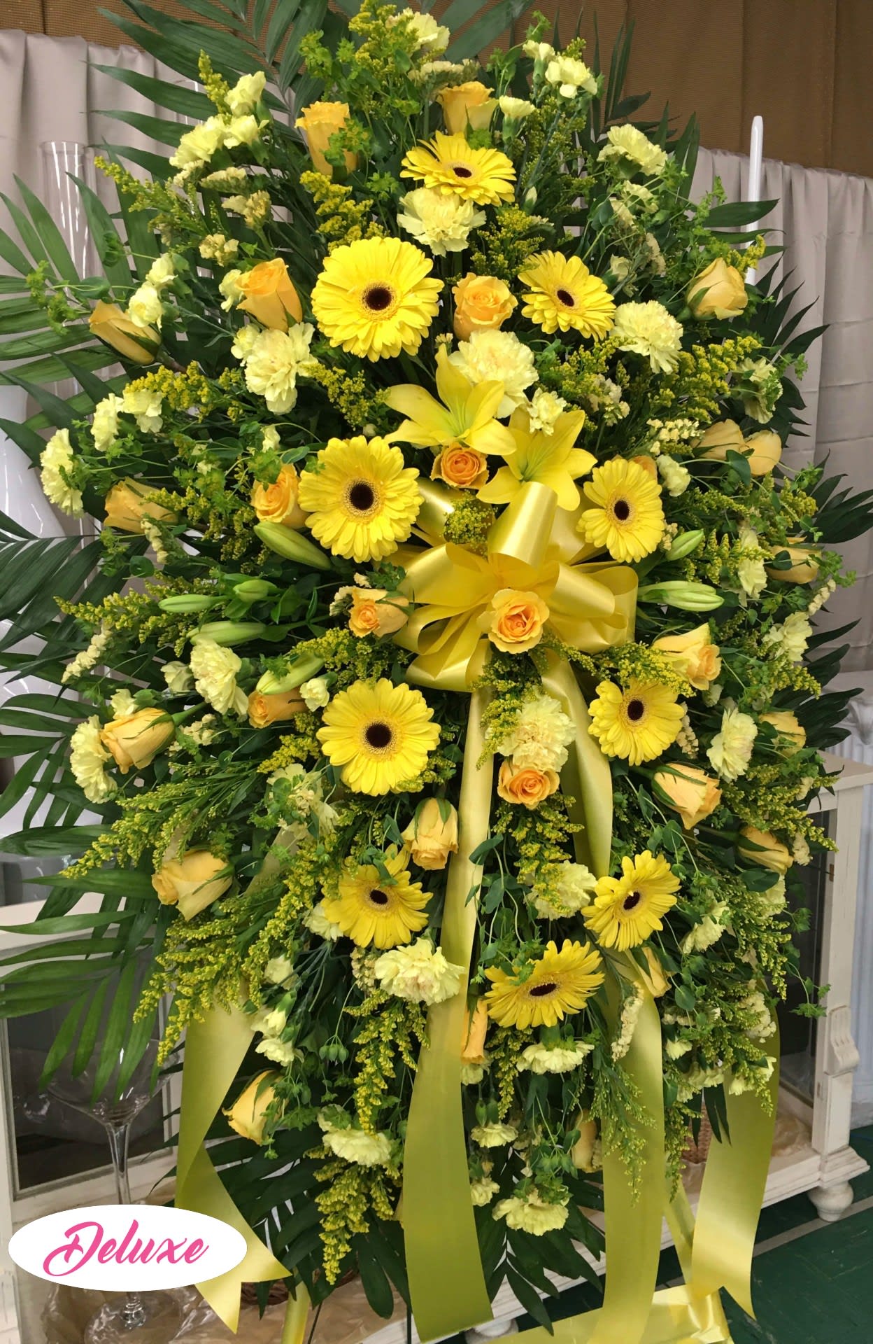 Large yellow floral standing spray with gerberas, roses, lilies, and ribbon