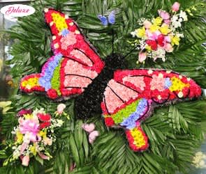 Butterfly-shaped floral tribute with colorful flower clusters on a green foliage background