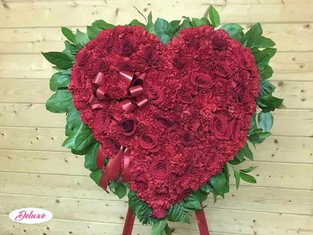 Heart-shaped red floral arrangement with ribbon accents and green leaves