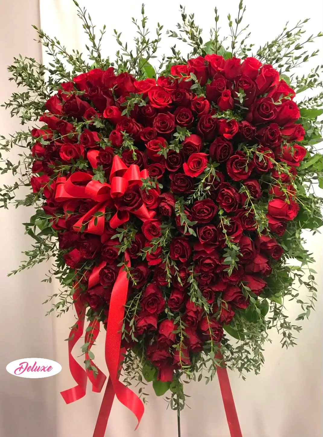 Heart-shaped red rose arrangement with red ribbon and greenery
