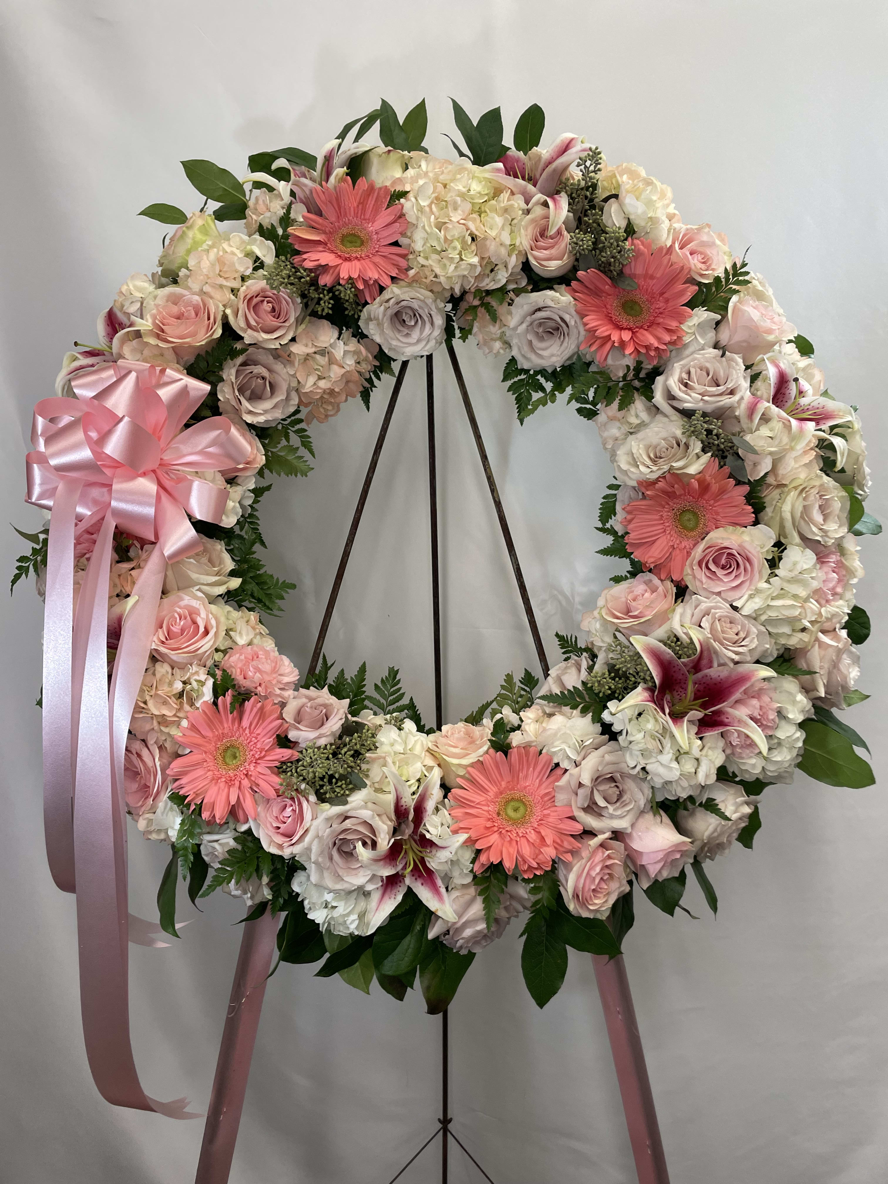Large pink and white floral wreath on a stand with ribbon bow