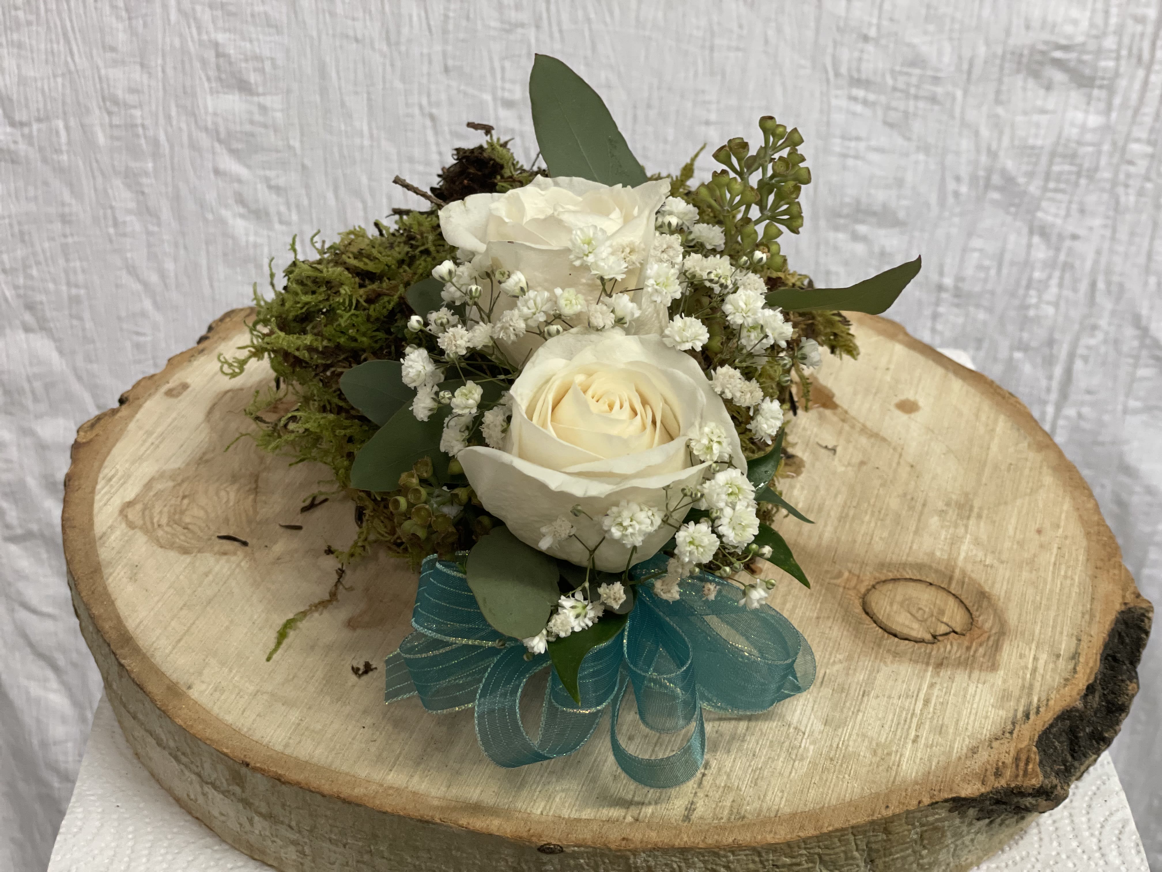 White roses with baby's breath and moss on a wood slice