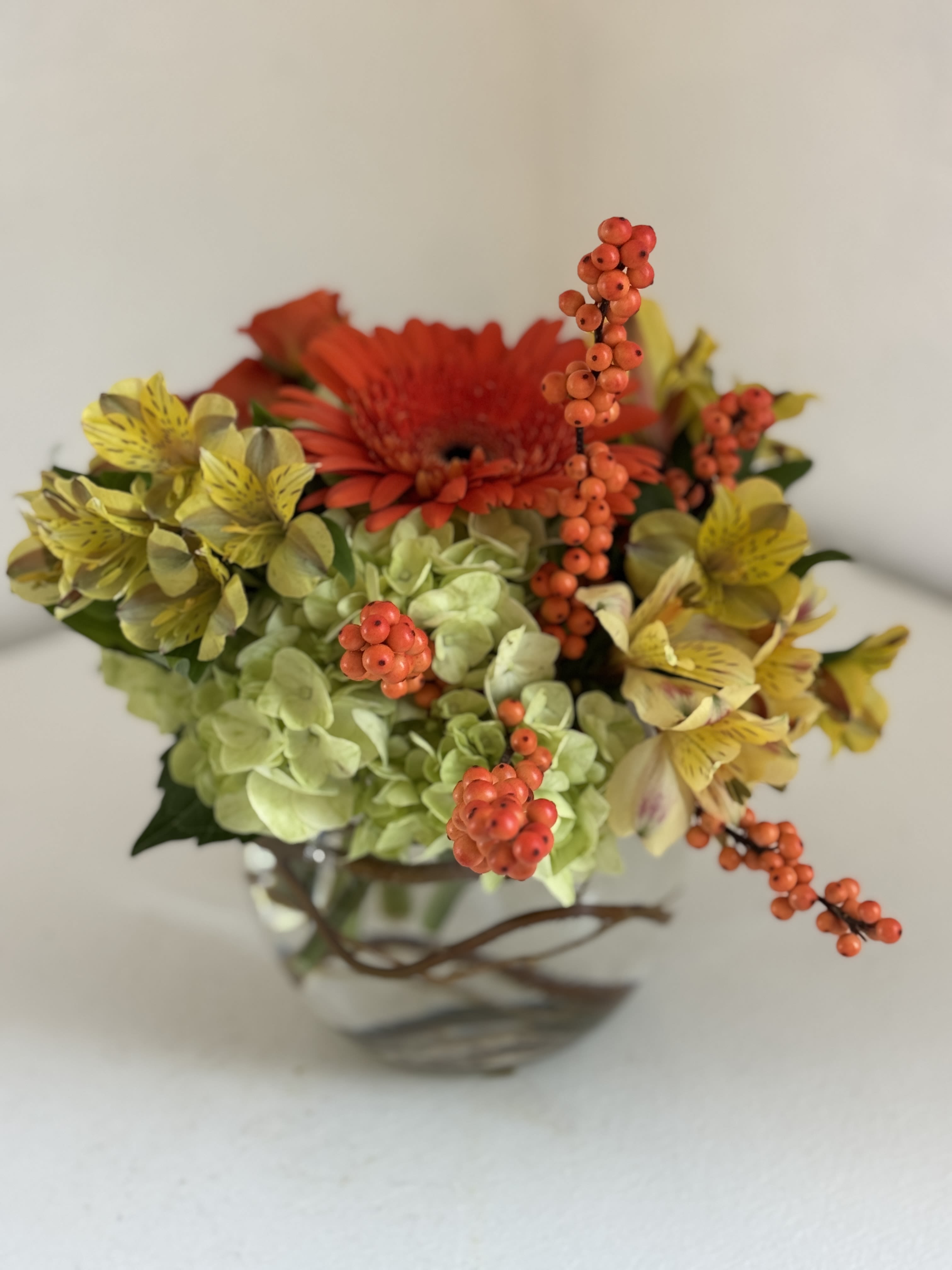 Mixed bouquet with orange gerbera, yellow alstroemeria, and green hydrangea in a glass vase