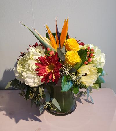 Autumn Paradise - This bountiful array of autumn blooms is arranged in a large clear glass gathering vase. With accents of our signature flower, the bird of paradise, is sure to please anyone for the holiday. 