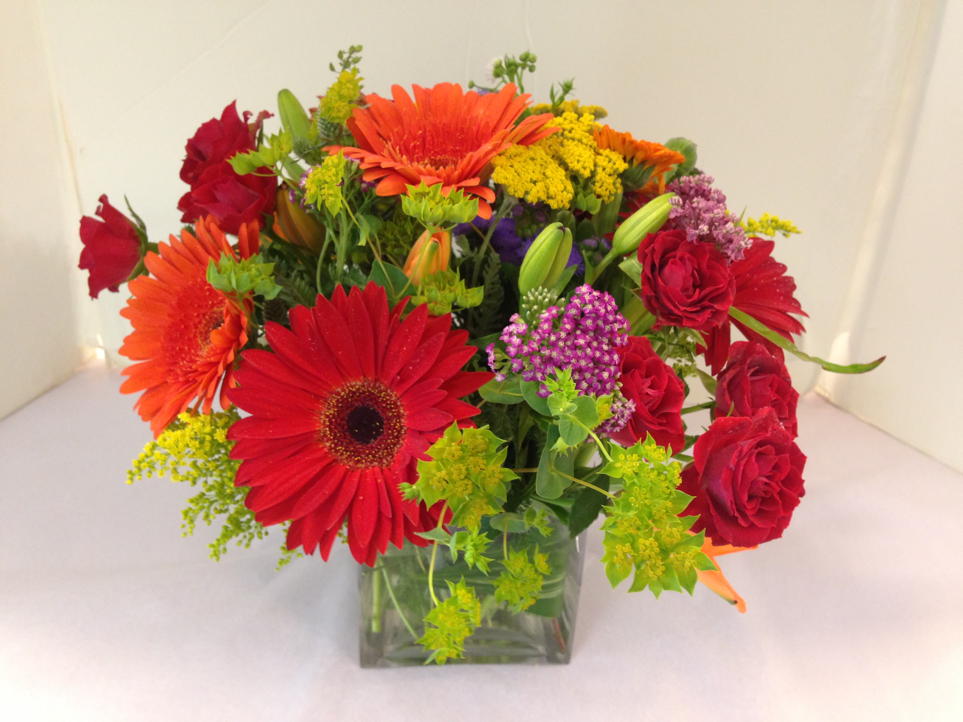 Mixed bouquet of red and orange flowers in a clear square vase