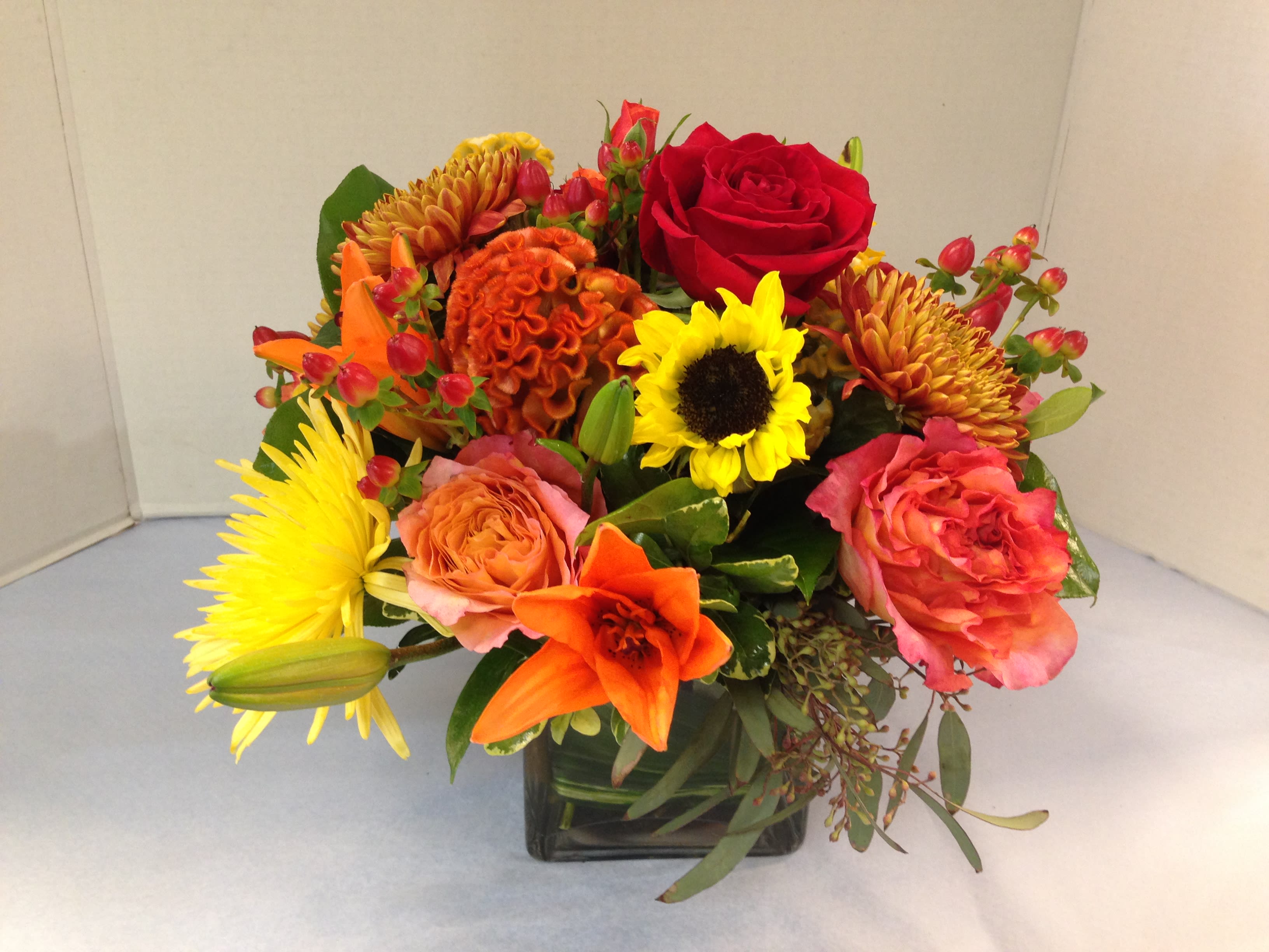 Mixed bouquet in a square glass vase with roses, lilies, and sunflowers