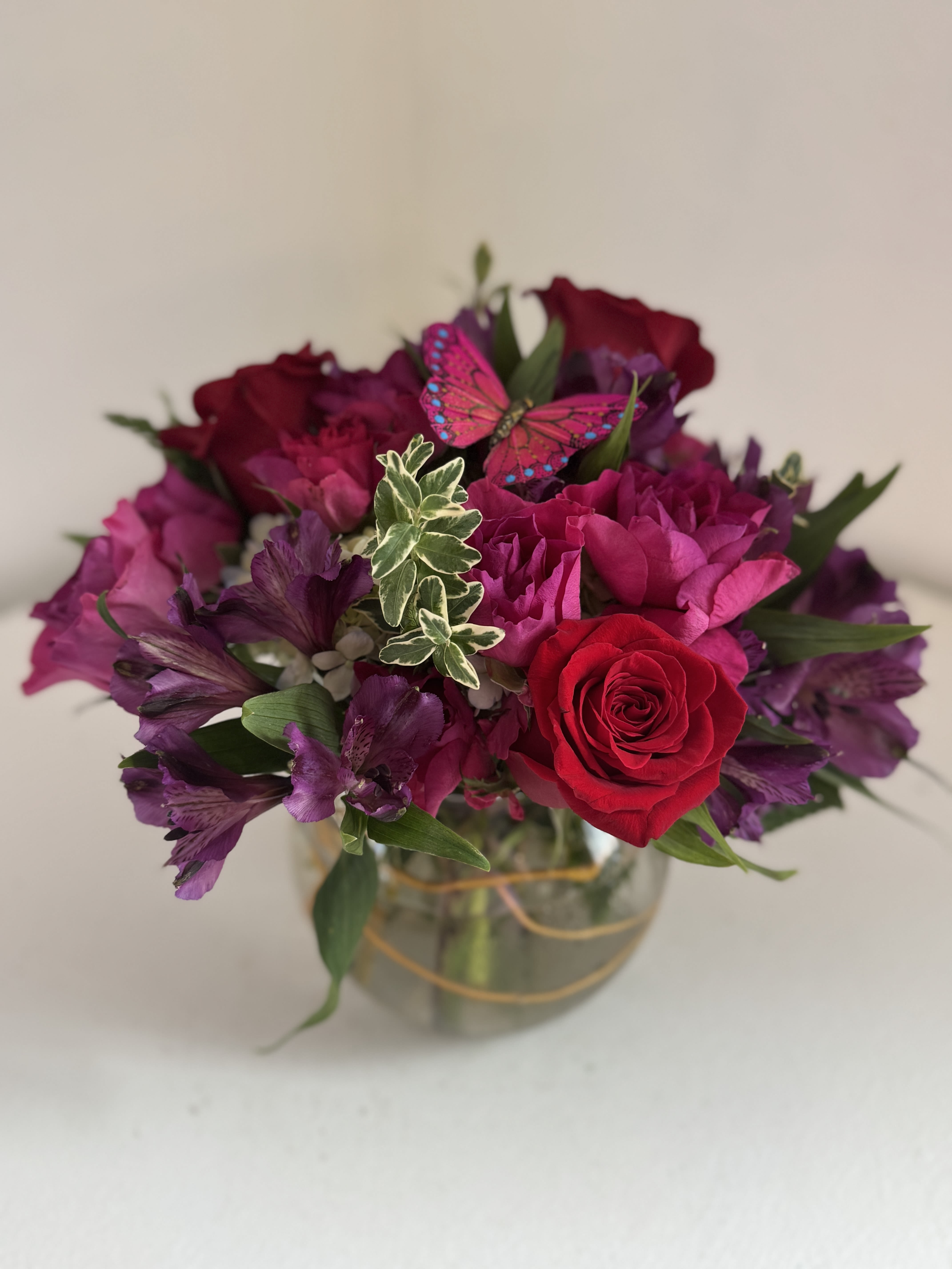 Bouquet of red roses and purple flowers in a glass vase with a butterfly decoration