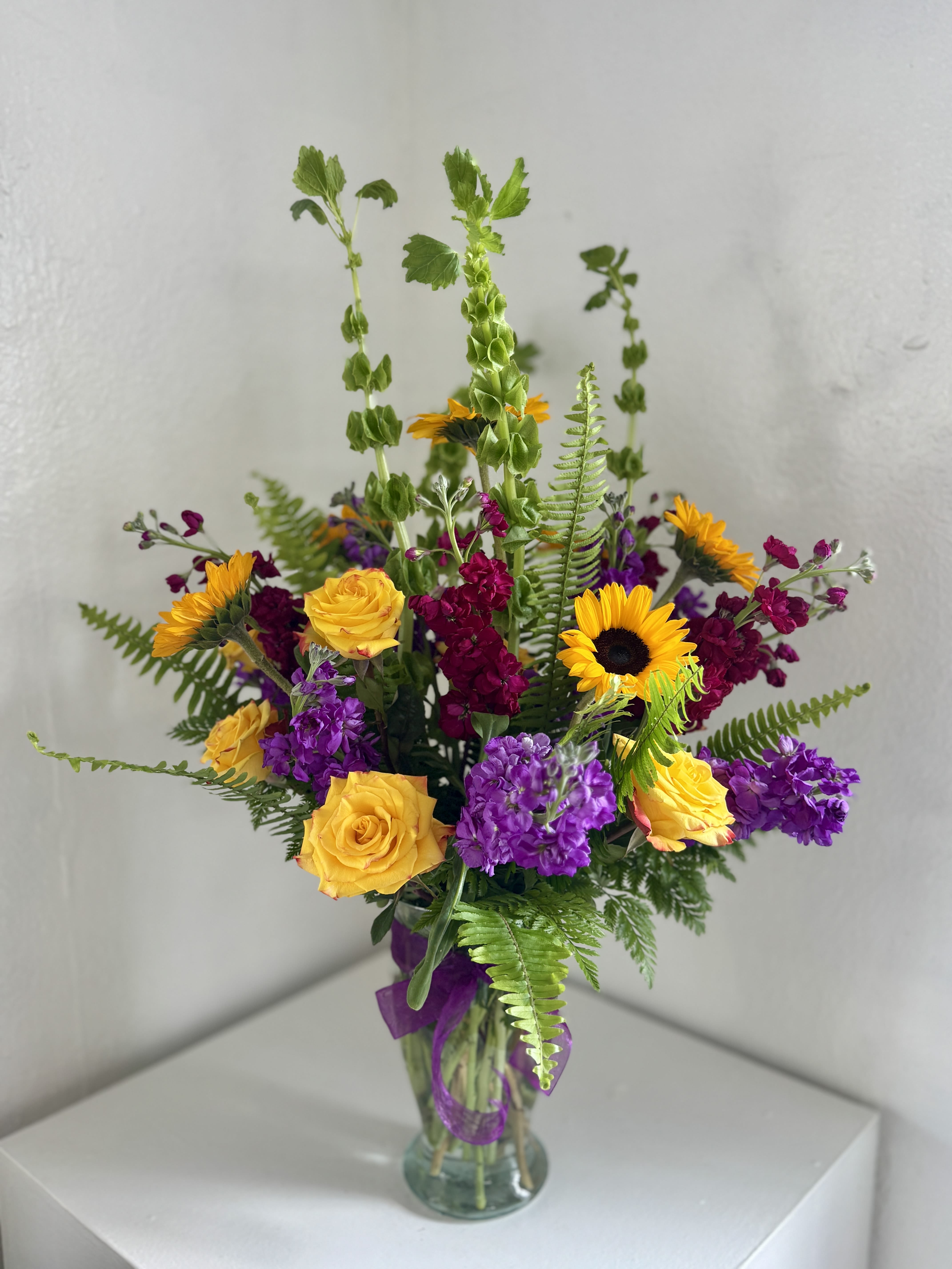 Mixed bouquet of yellow roses, sunflowers, and purple flowers in a glass vase