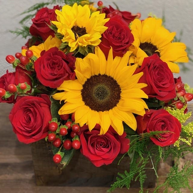 Bouquet of red roses and yellow sunflowers in a square vase